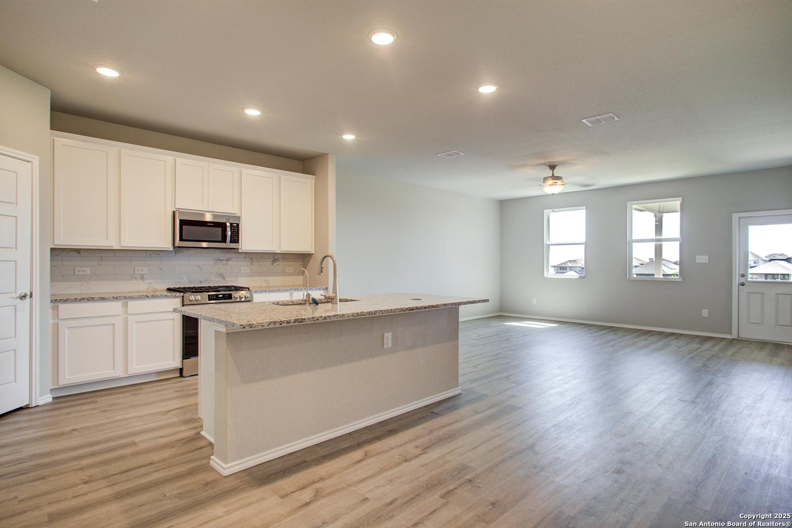 Bright open-concept kitchen with white cabinets, granite island, and stainless microwave in Davidson Homes The Douglas G, San Antonio