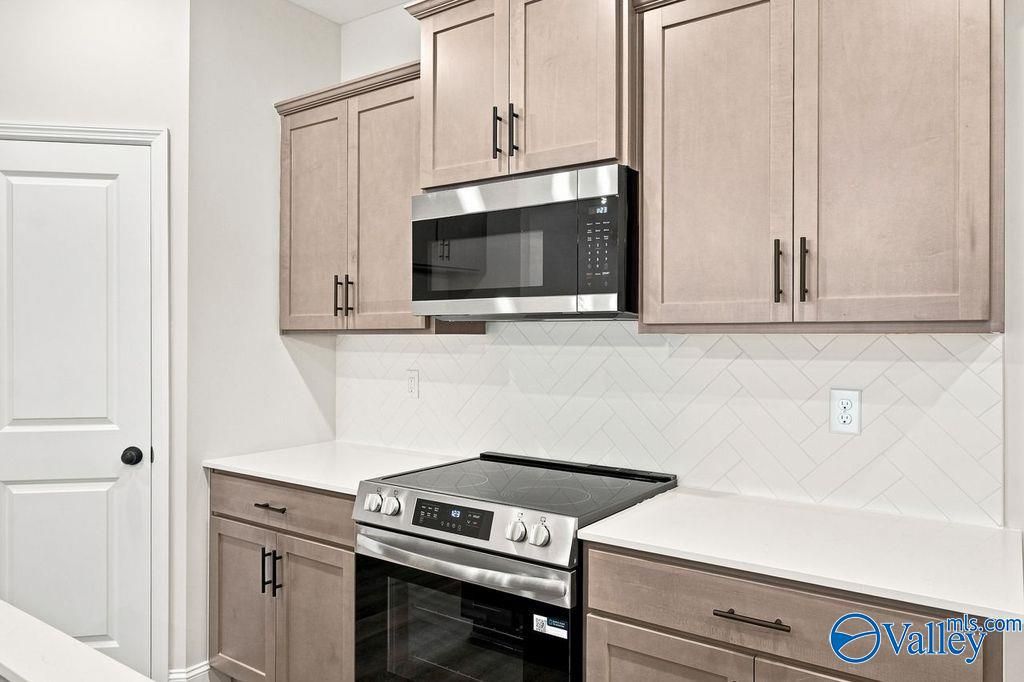 Modern kitchen with light wood cabinets, white countertops, and herringbone backsplash in The Camilla C floor plan, Hartselle.