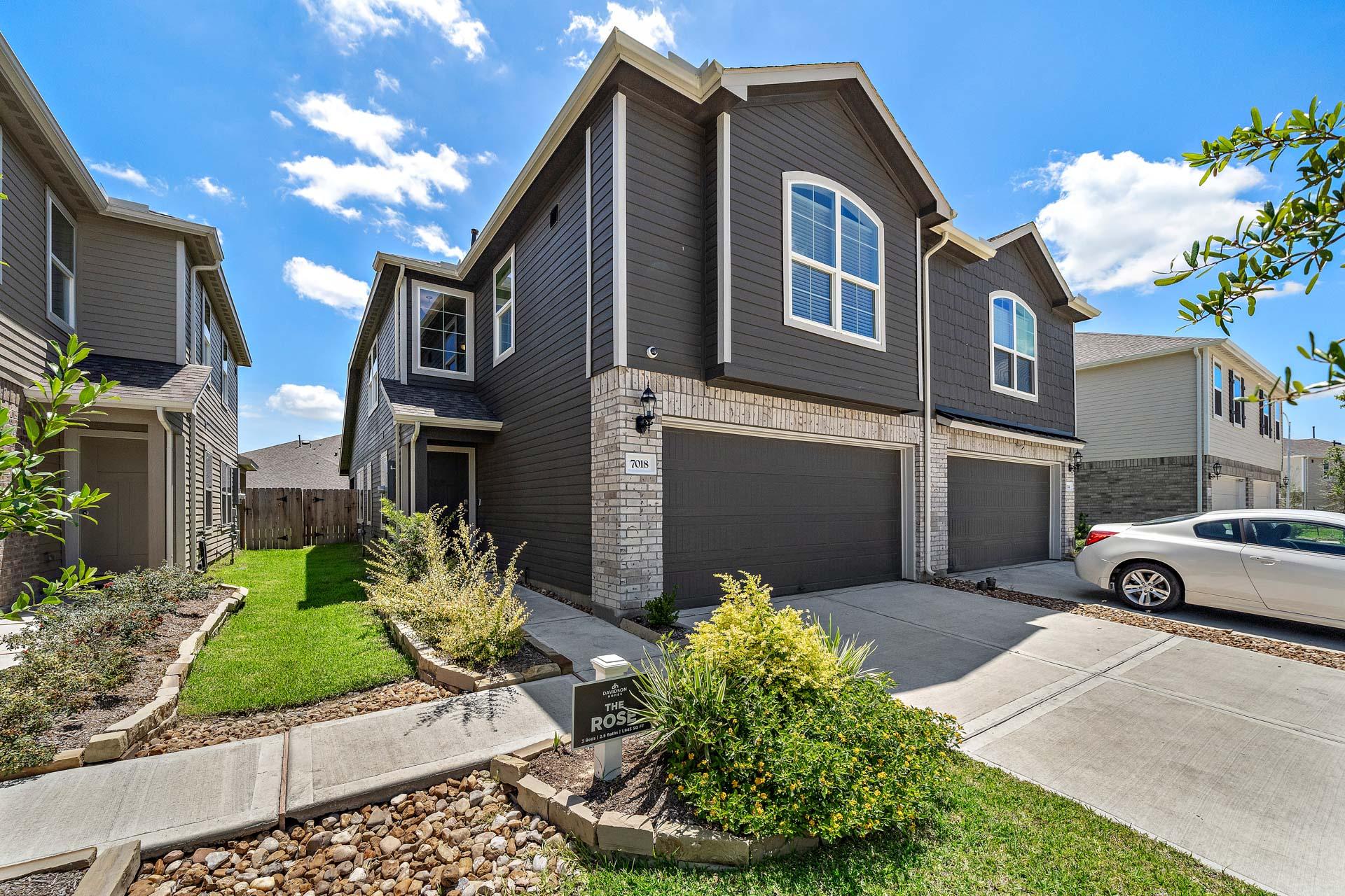 Modern gray townhomes at Haven at Kieth Harrow in Cypress Texas with brick accents, double garages, and lush landscaping