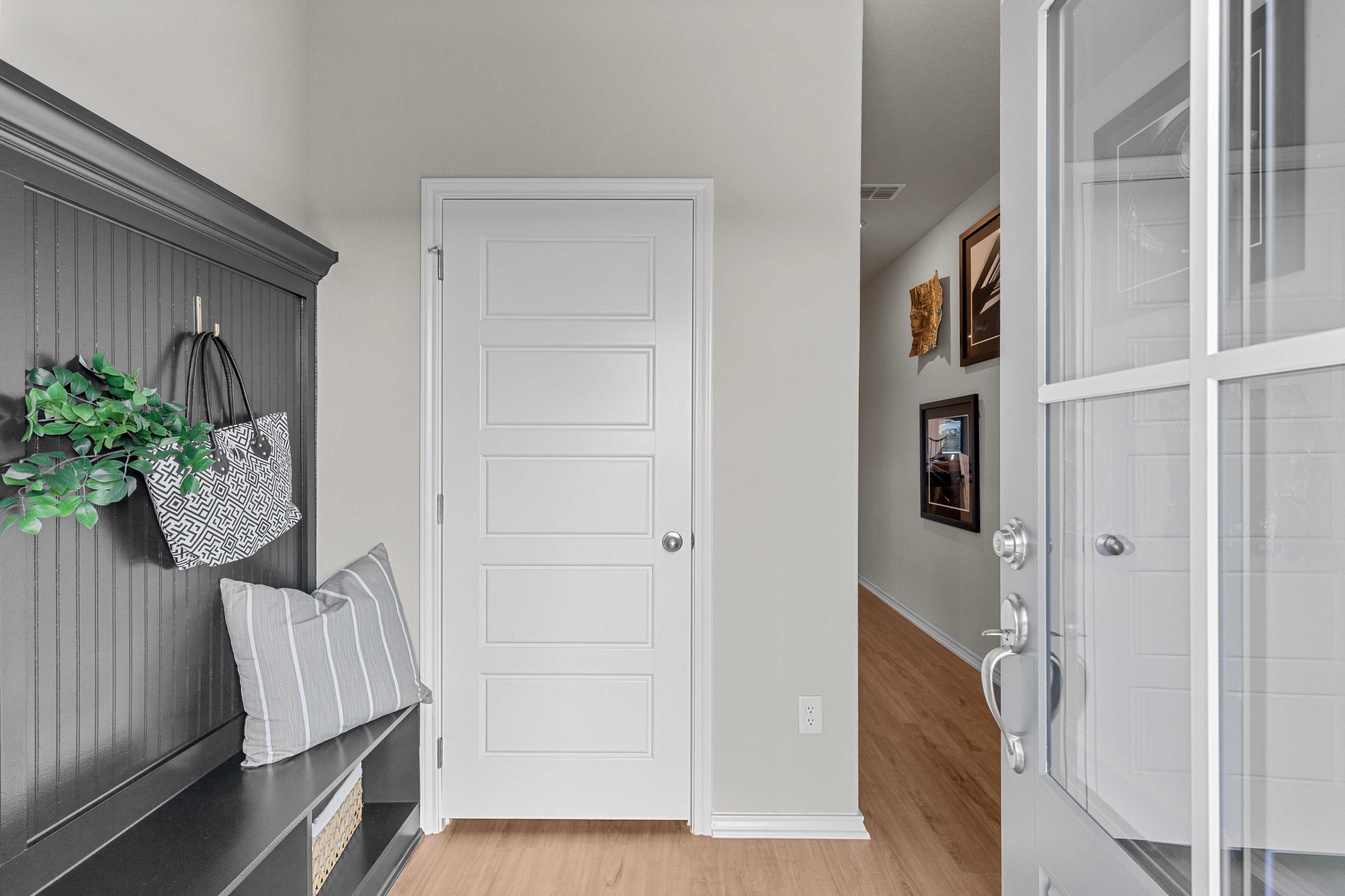 Spacious entryway in The Sabine C featuring gray built-in bench, coat hooks, white door, and glass front entry, Davidson Homes San Antonio