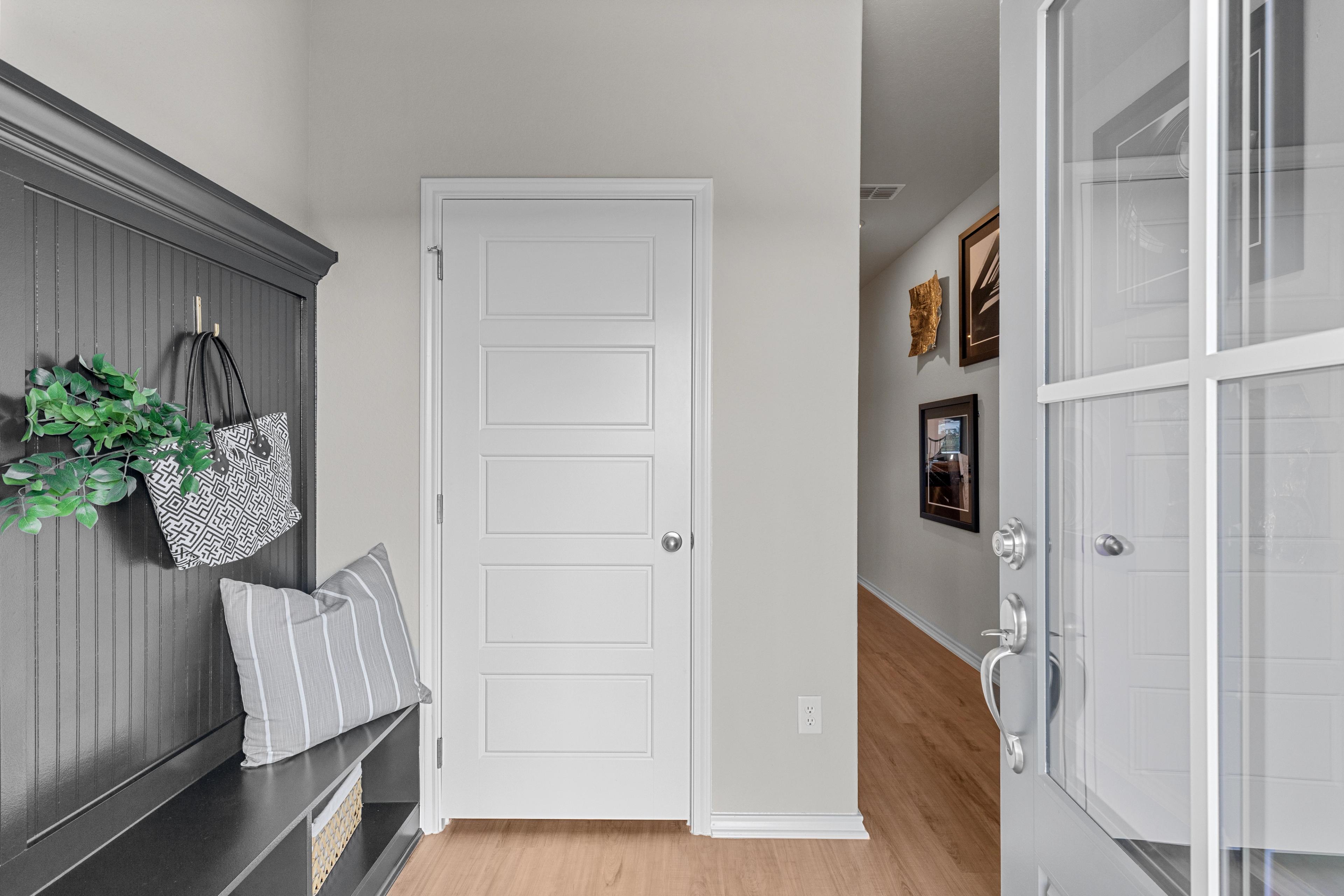 Cozy entryway in The Sabine B home with built-in gray bench, coat hooks, purse, and white paneled door