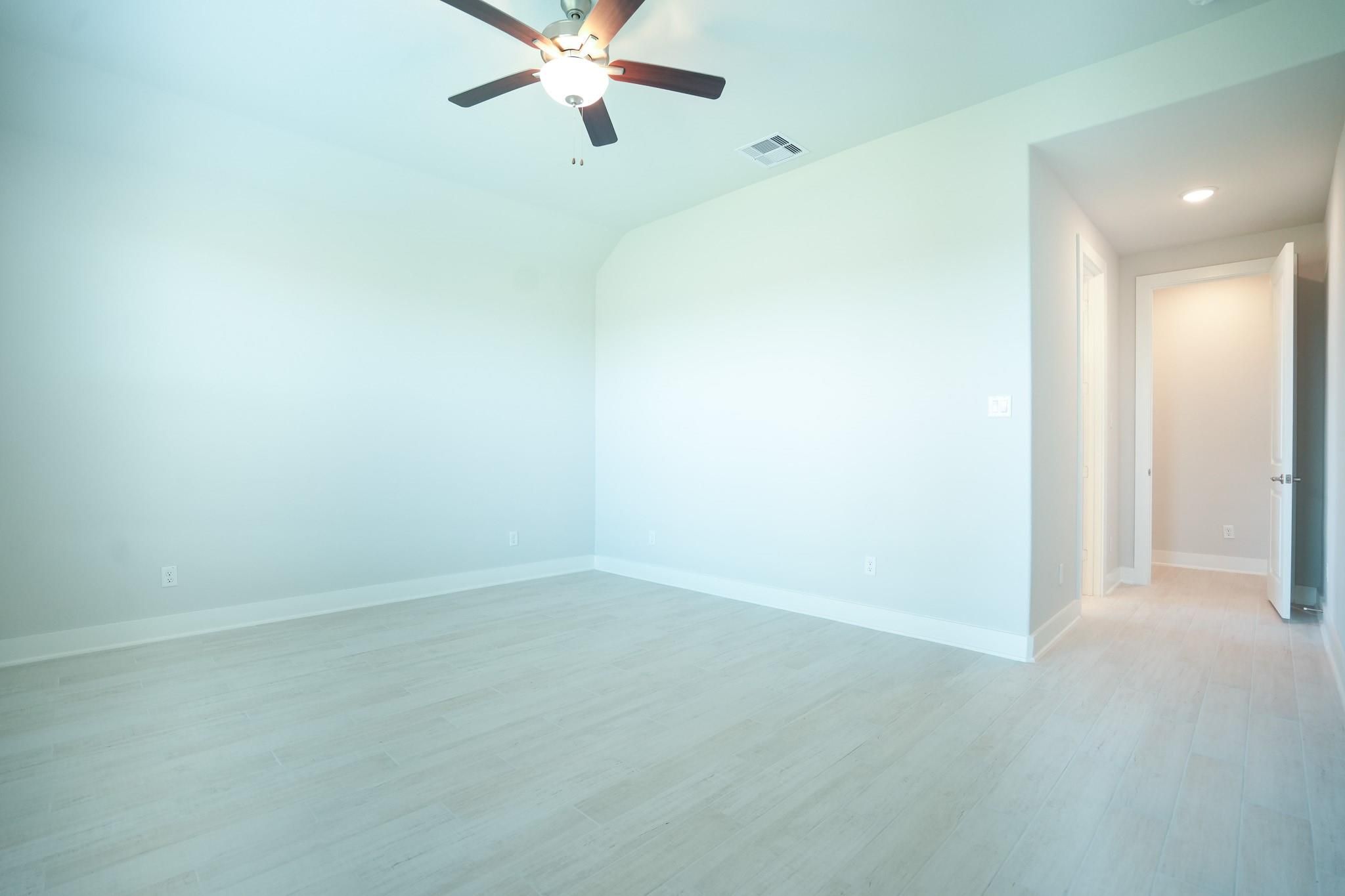 Bright empty bedroom with ceiling fan, neutral walls, and laminate flooring in Davidson Homes The Edward C, Lago Mar, Texas City