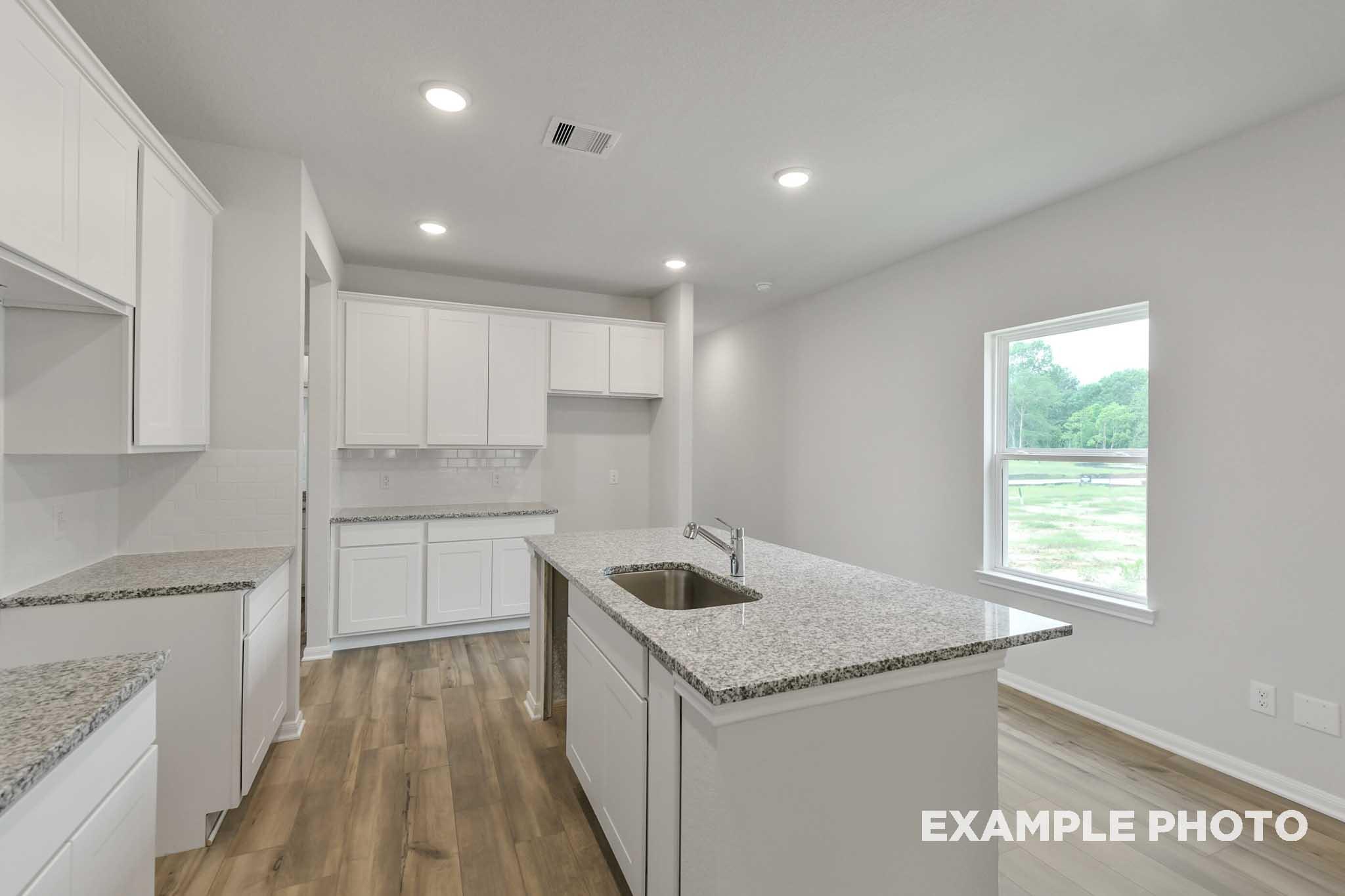 Modern kitchen in The Frio featuring white cabinetry, granite countertops, and a central island in a Conroe, Texas home.