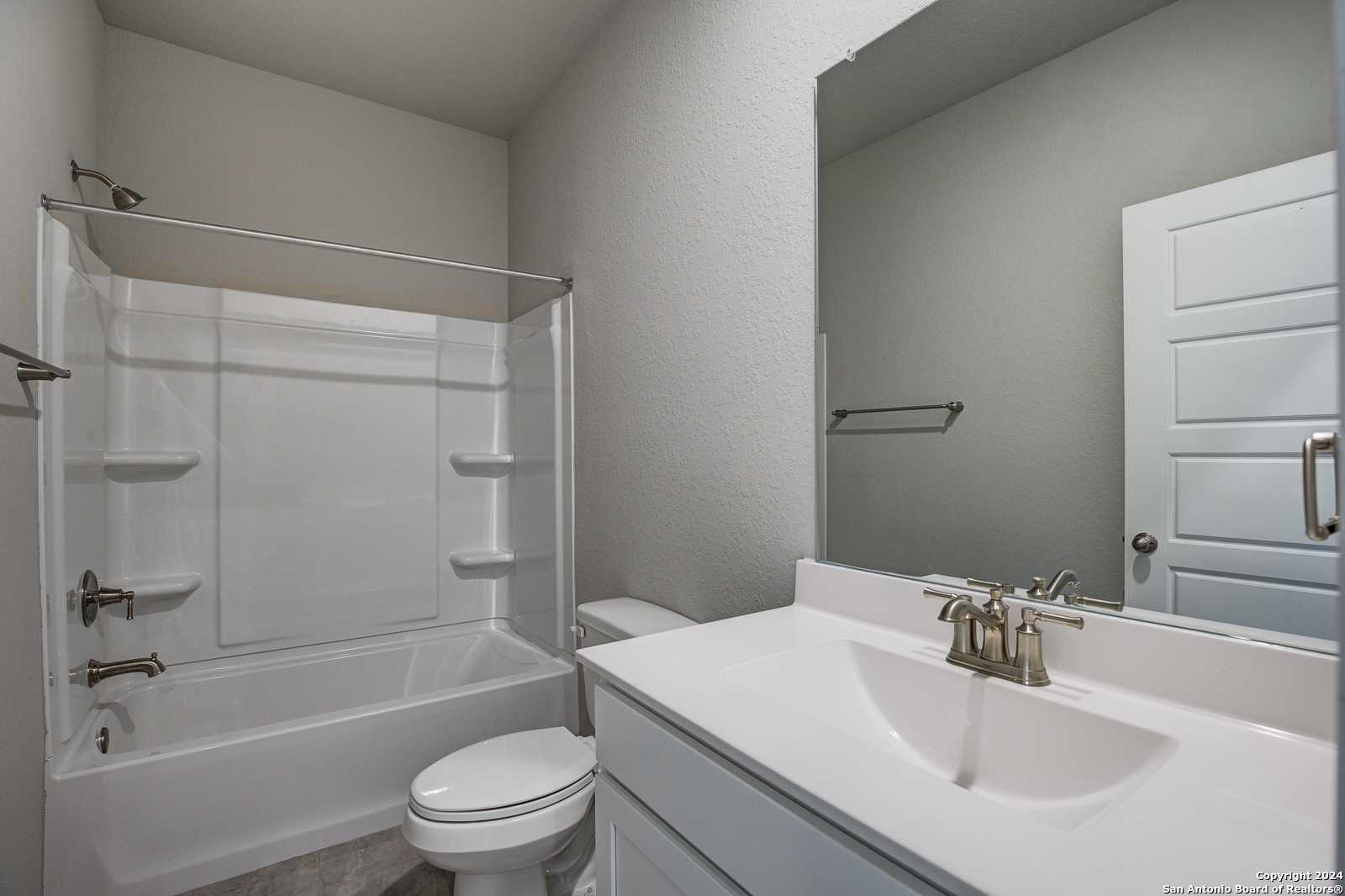 Bright guest bathroom with white tub/shower combo, glass enclosure, single vanity sink, and large mirror in Davidson Homes Daphne J, Seguin, Texas