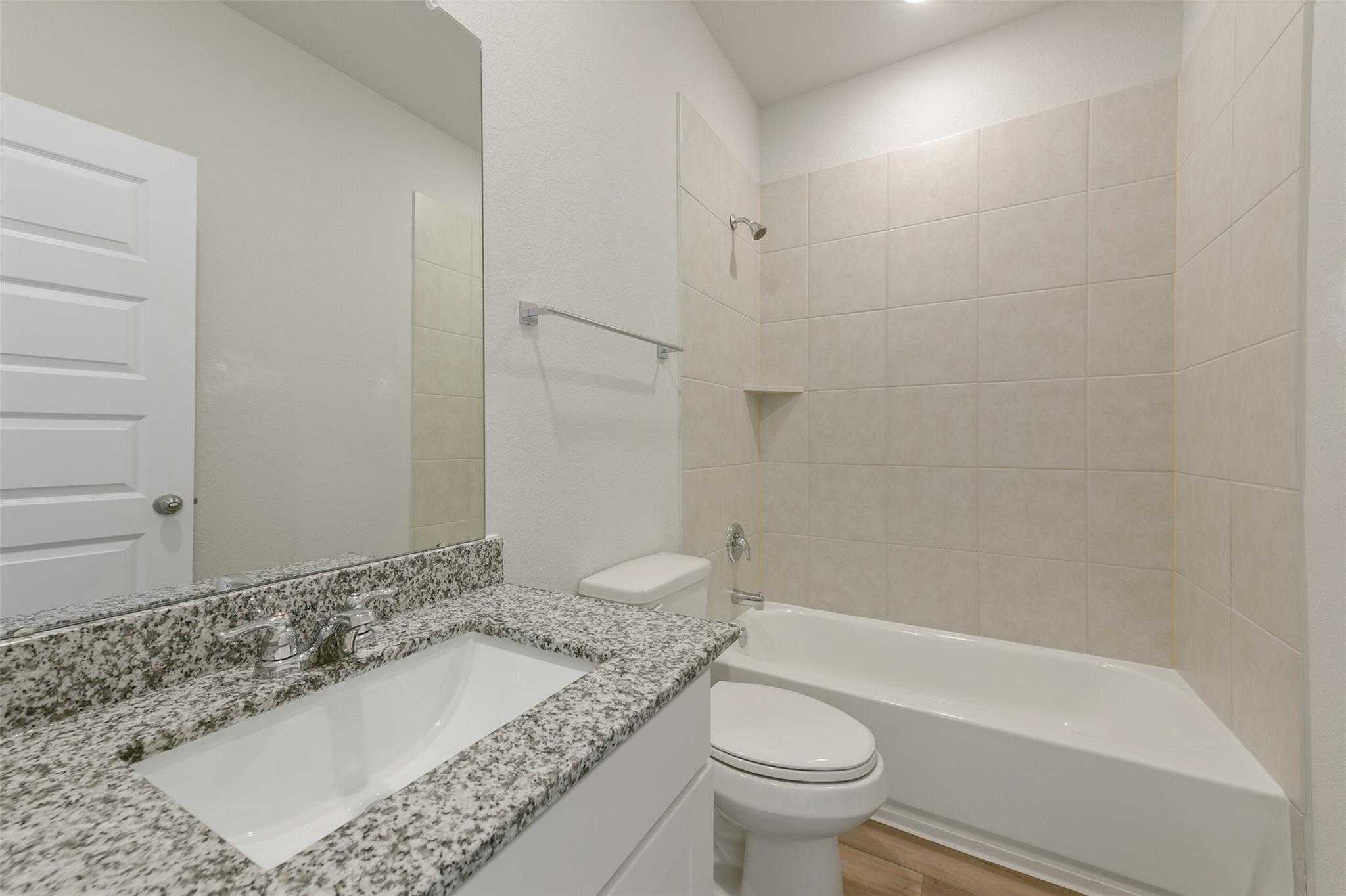 Modern bathroom with granite vanity, soaking tub, tiled shower, and wood flooring in Davidson Homes The Laguna B, Dayton, Texas