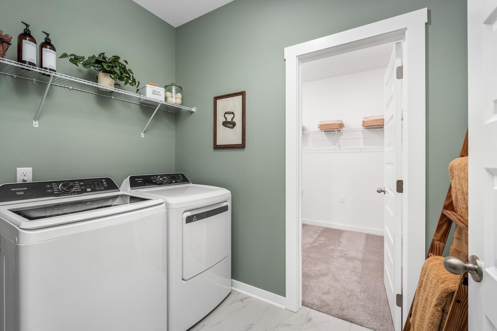 Spacious laundry room at Calista Farms in White House TN with green walls, white washer dryer, utility shelves and adjacent closet