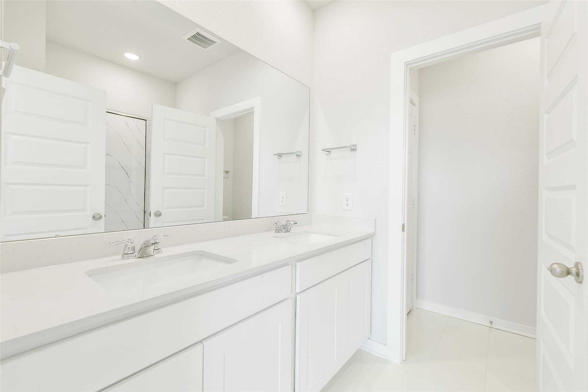 Modern master bathroom with double white vanity, quartz counters, and large mirror in Davidson Homes San Marcos E, Cleveland TX