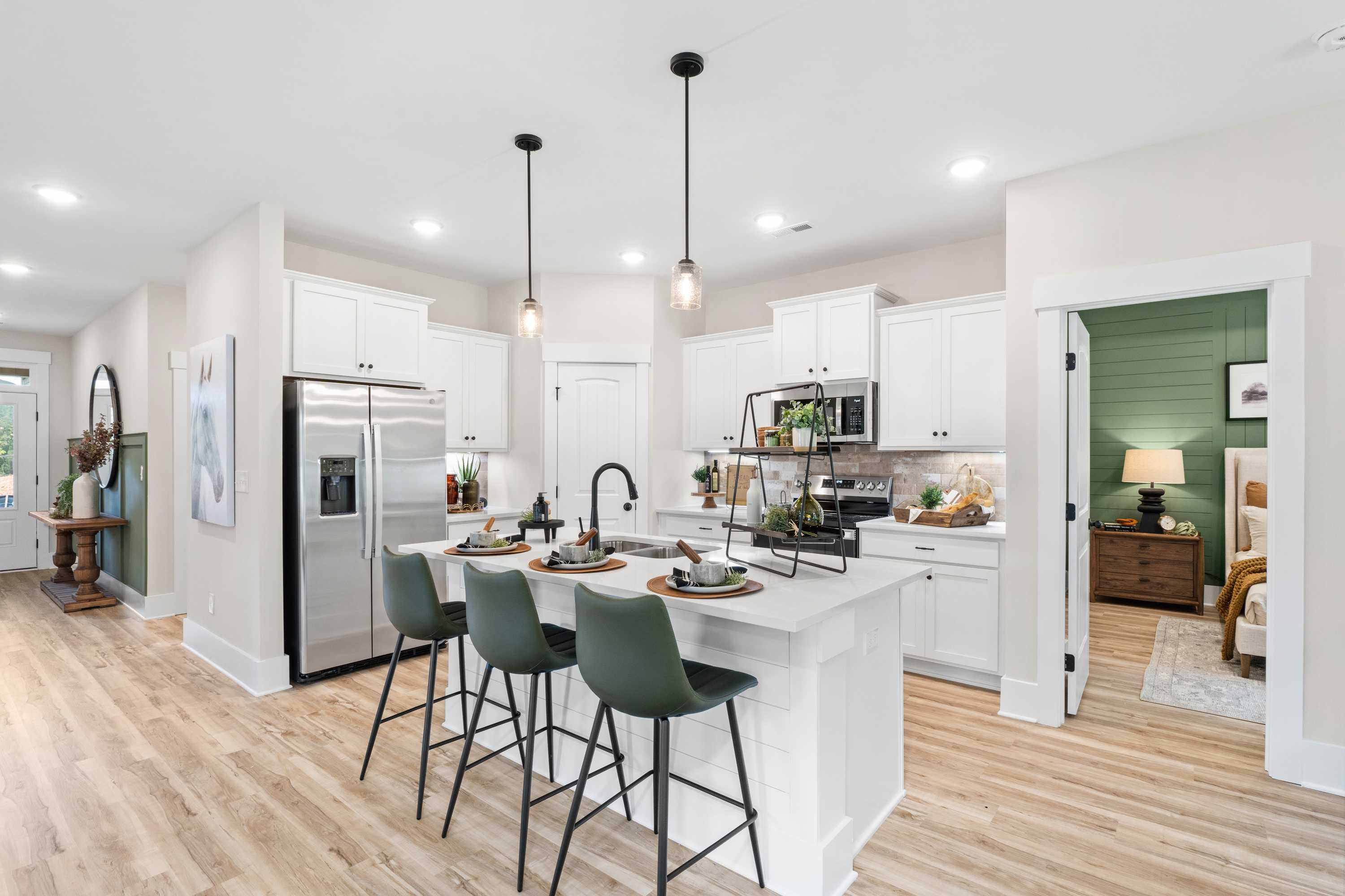 Modern kitchen at Spragins Cove in Huntsville AL with white island, green bar stools, stainless appliances, and hardwood floors