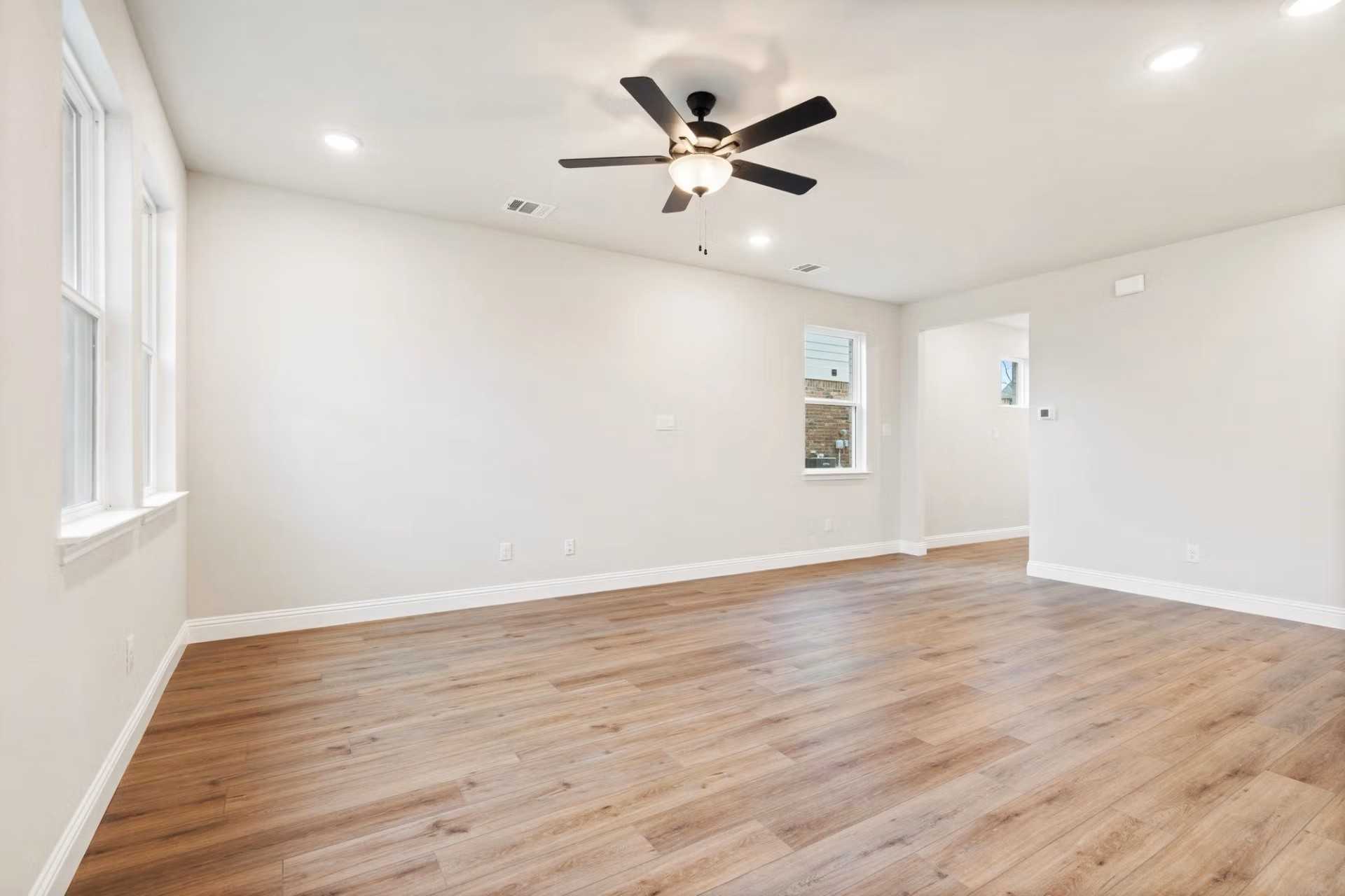 Bright open living room with hardwood floors, white walls, and dual ceiling fans in Davidson Homes The Wake D, Wylie, Texas