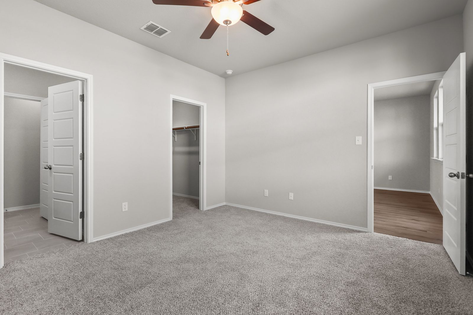 Spacious bedroom in The Arroyo A featuring plush carpeting, a ceiling fan, and walk-in closet access.