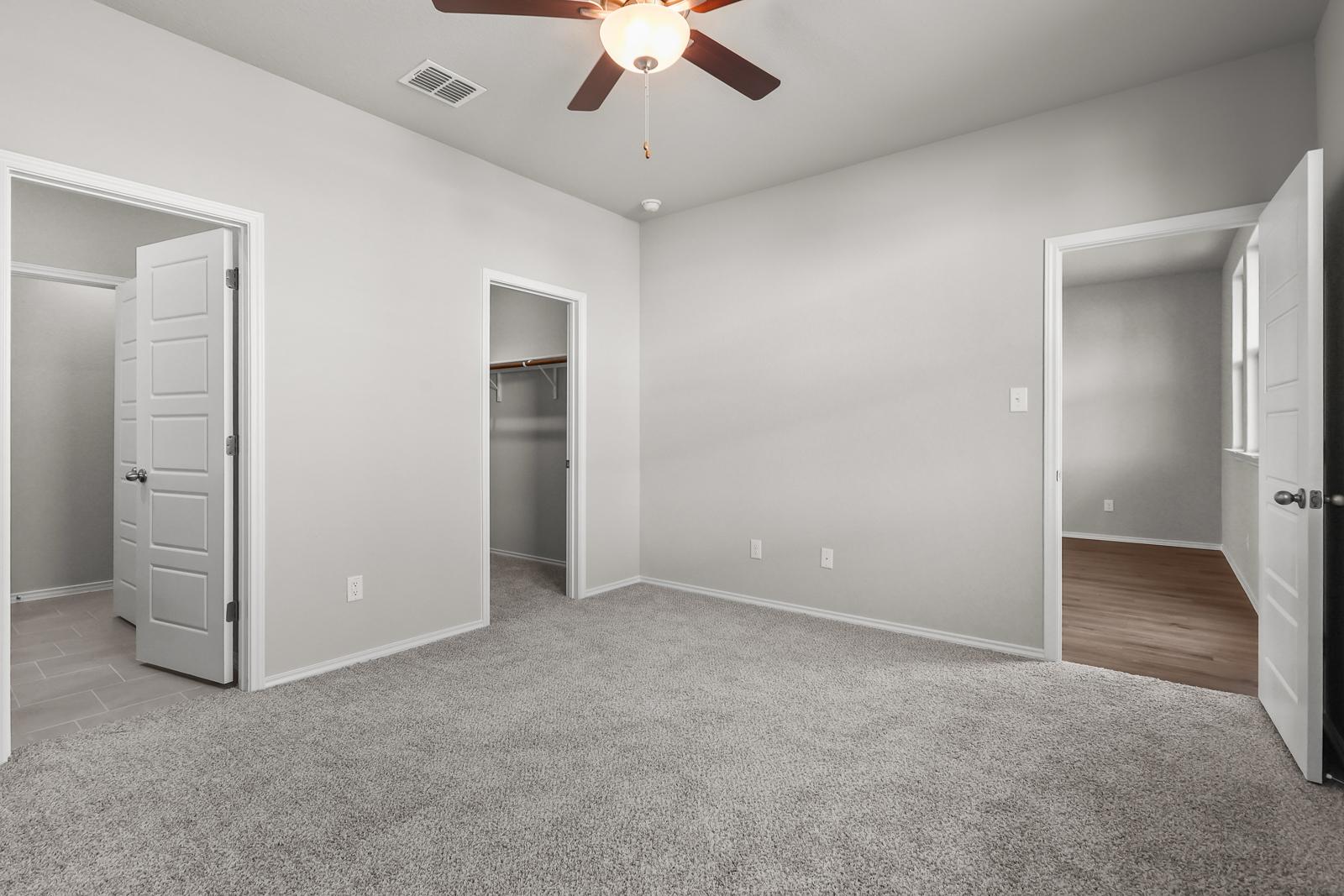Spacious bedroom in The Arroyo A featuring plush carpeting, a ceiling fan, and walk-in closet access.