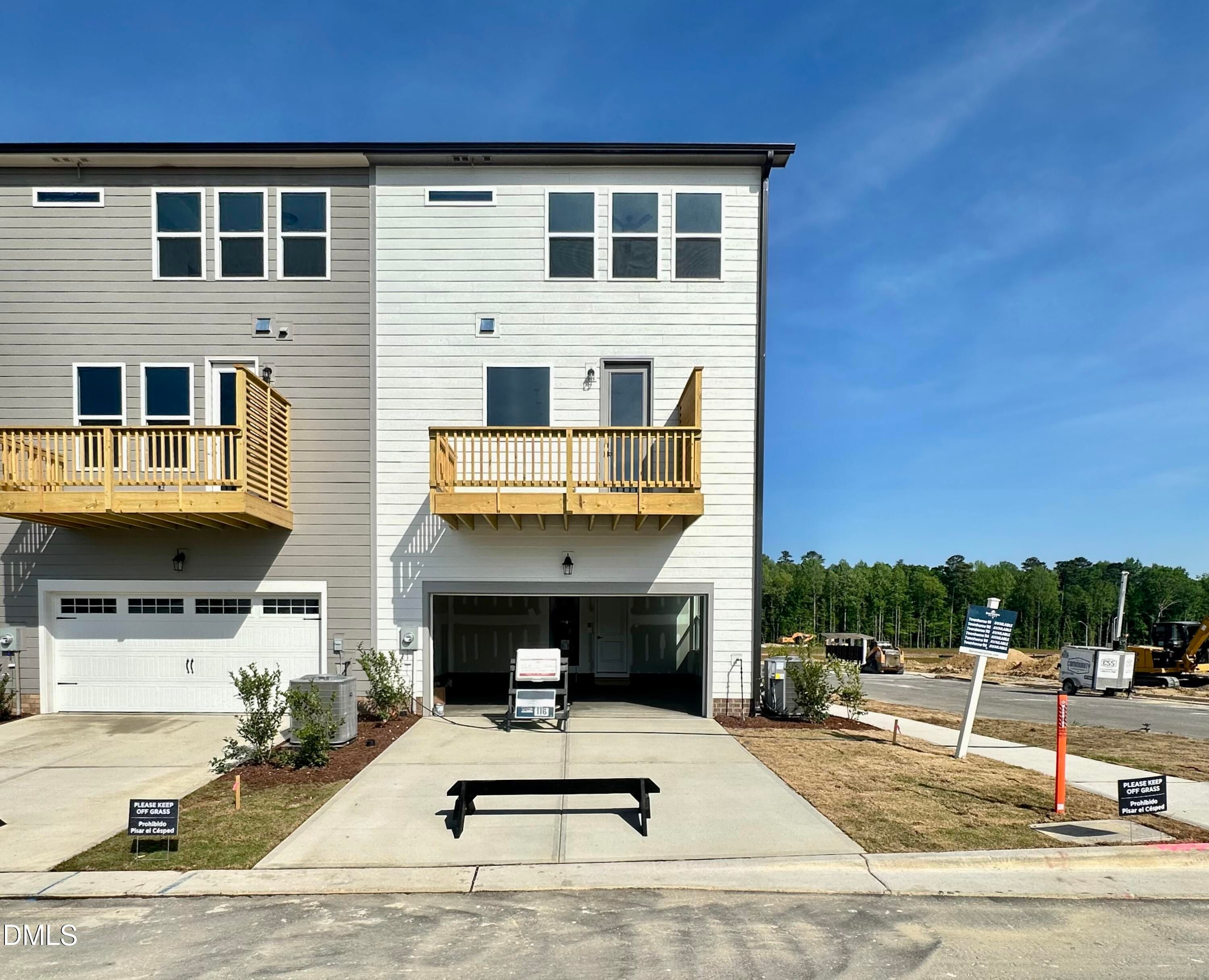 Modern 3-story townhome exterior with wooden balcony, open 2-car garage, and driveway in Forestville Yard Townhomes, Knightdale, NC