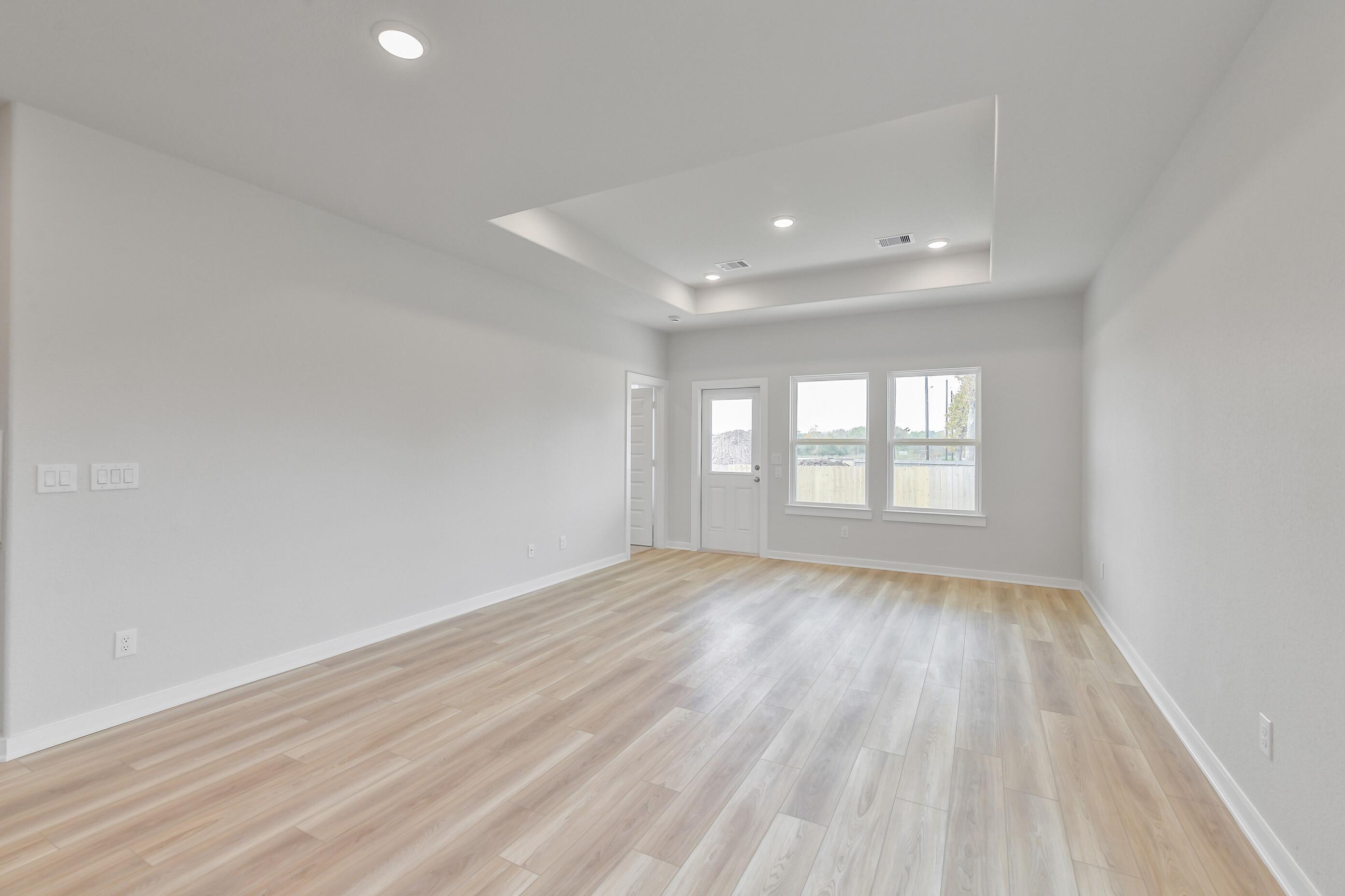 Bright living room with tray ceiling, light hardwood floors, and French doors to backyard in Davidson Homes Colorado G, Magnolia Texas