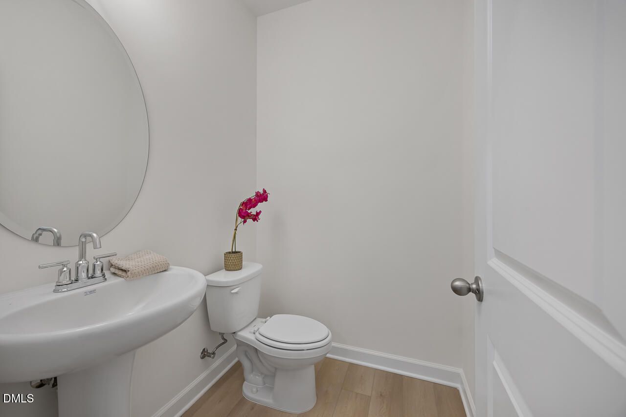 Elegant powder room with pedestal sink, round mirror, and wood-look flooring in Davidson Homes The Magnolia A, Wendell Ridge