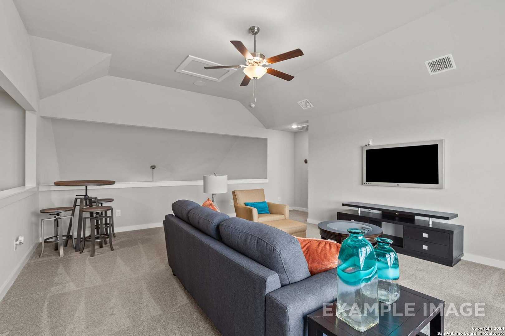 Cozy living room with blue sectional sofa, mounted TV, bar stools, and ceiling fan in The Collin B floor plan, Seguin, Texas