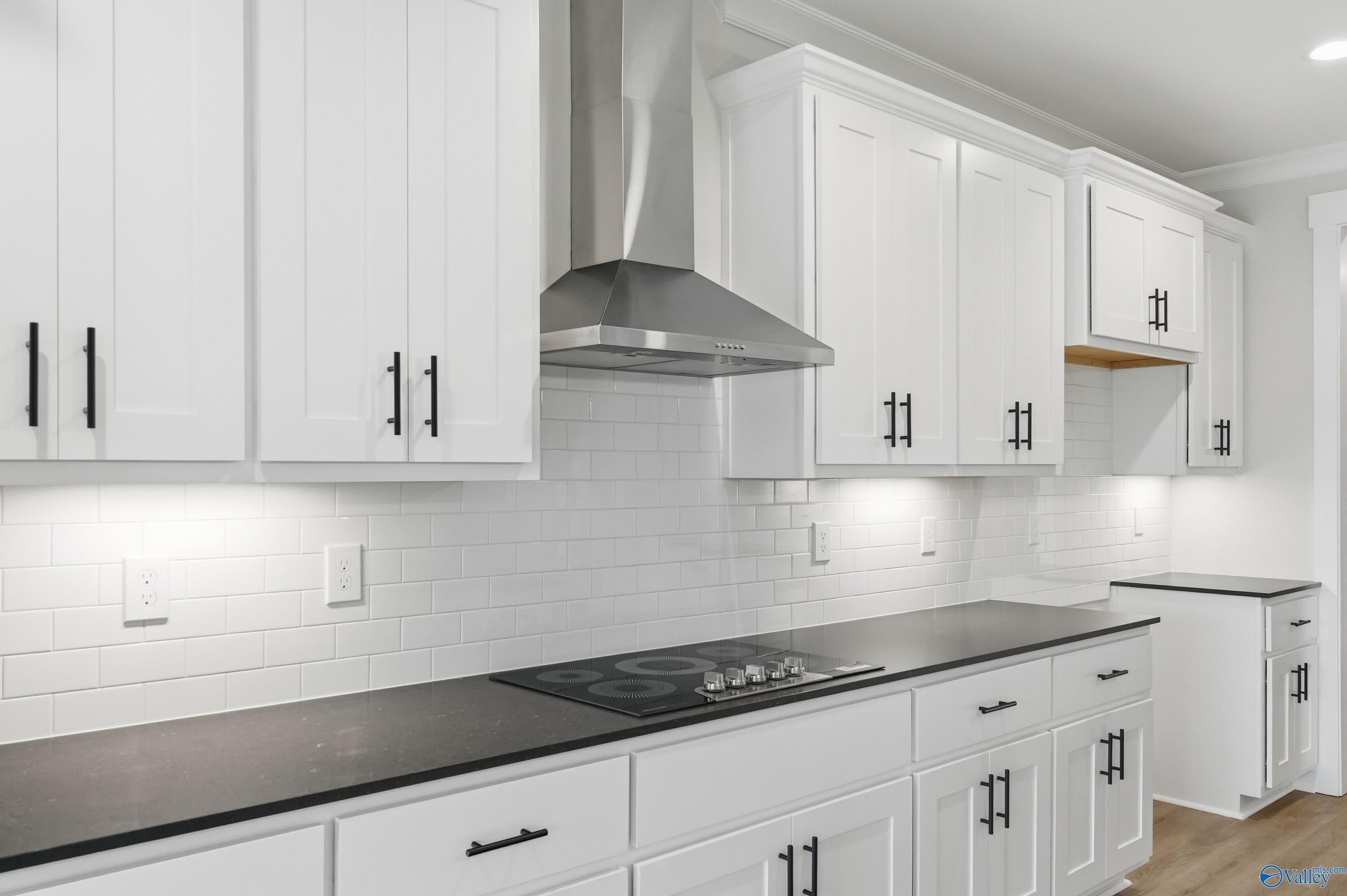 Modern white shaker kitchen with black quartz counters, gas cooktop, stainless hood, subway backsplash in The Finleigh, Meridianville, AL