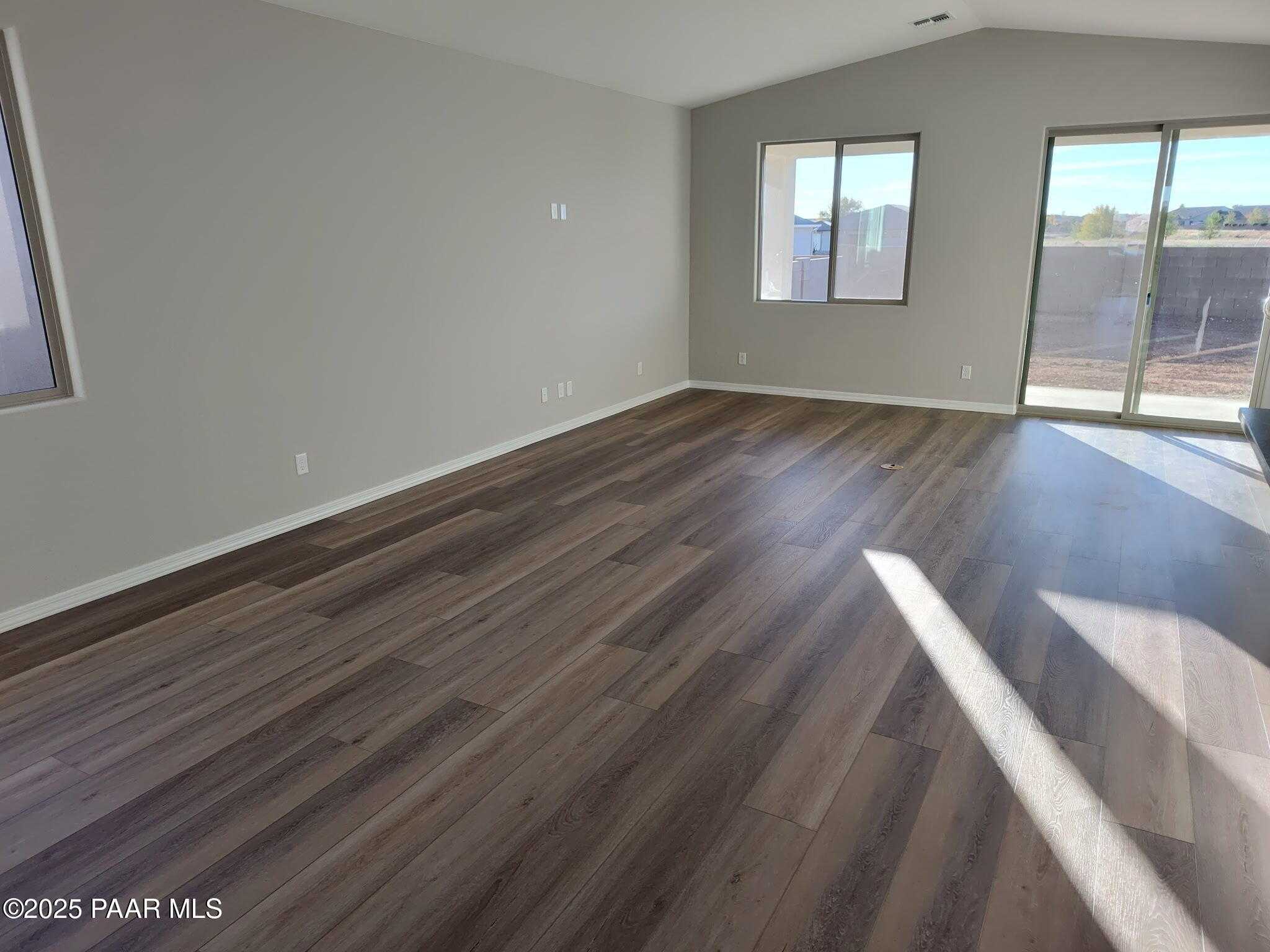 Bright spacious living room with vaulted ceiling, large windows, sliding patio doors, and luxury vinyl plank flooring in Davidson Homes The Frontier C, Prescott Valley