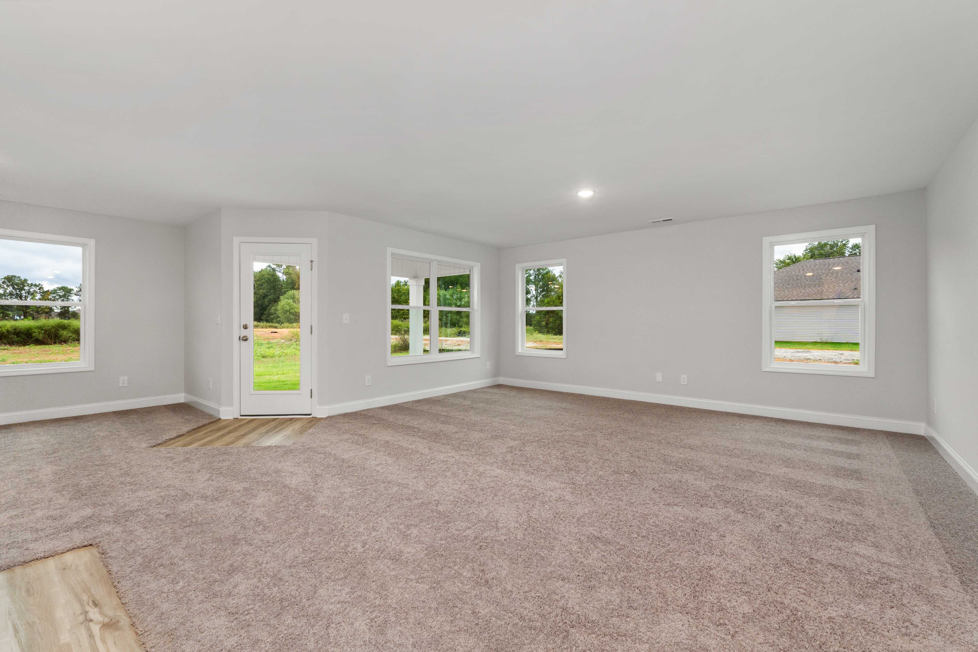 Spacious empty living room at Collins Lane in Meridianville AL with large windows, neutral carpet and green yard view