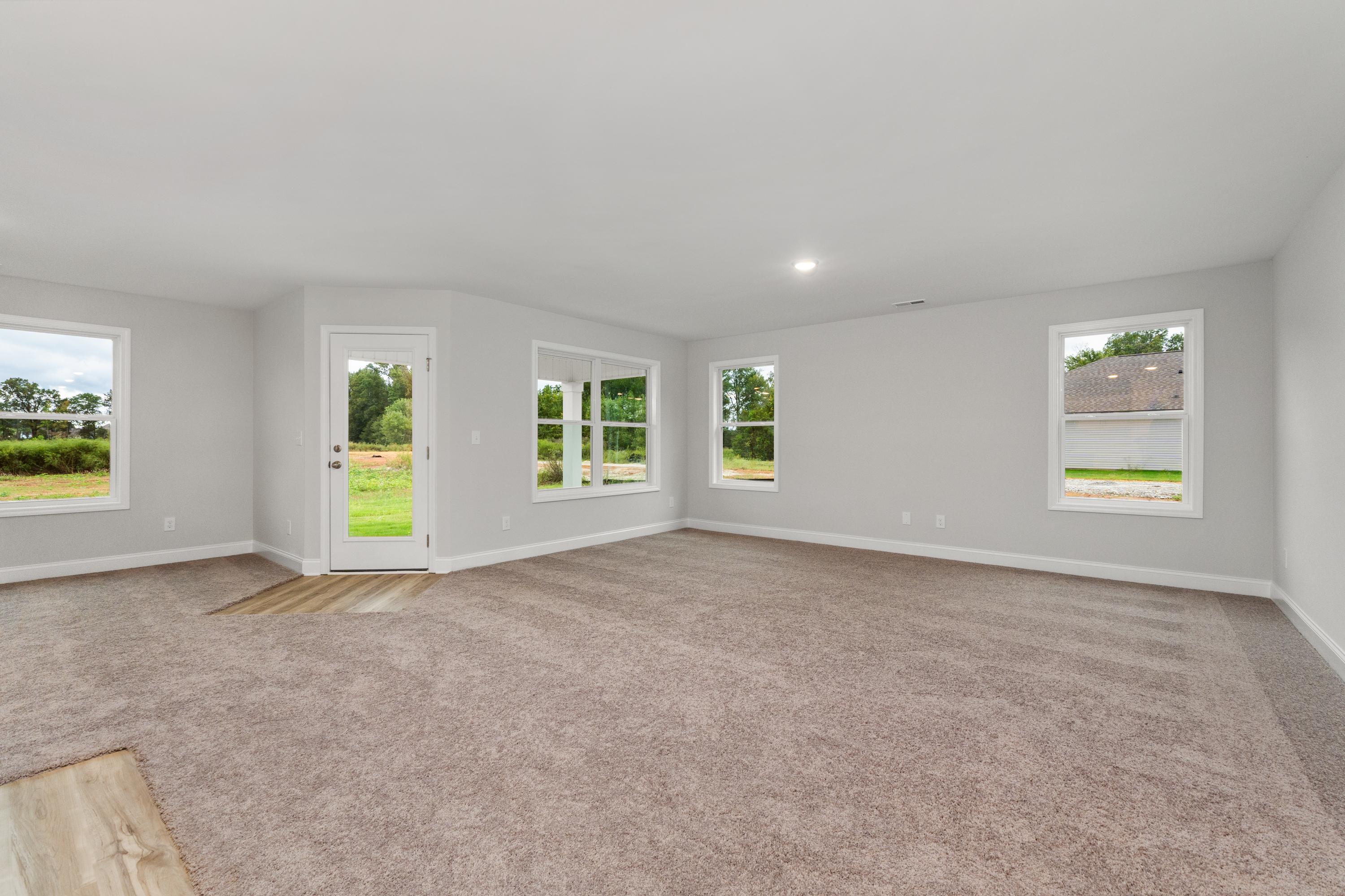 Spacious empty living room at Collins Lane in Meridianville AL with large windows, neutral carpet and green yard view