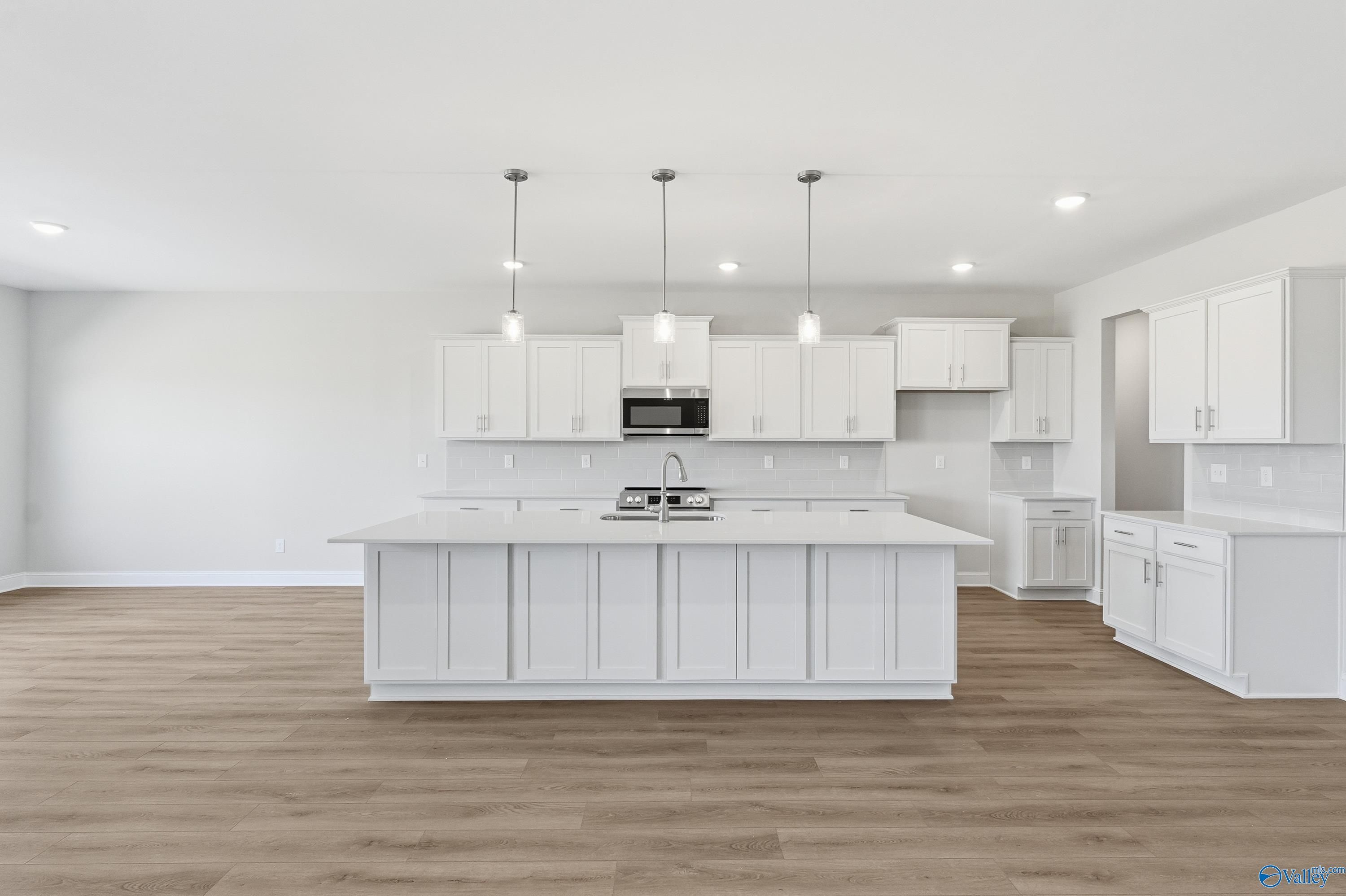 Bright white kitchen with large island, pendant lights, and stainless microwave in Davidson Homes The Finleigh, Harvest, Alabama