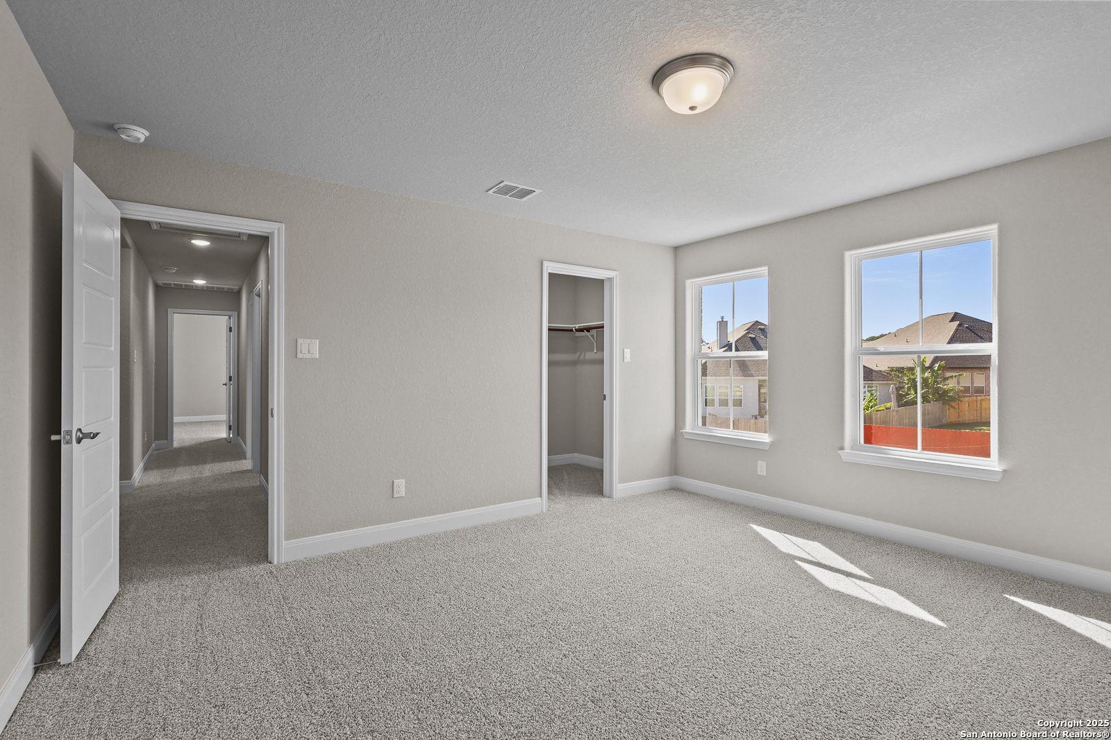 Bright secondary bedroom with open walk-in closet, neutral gray walls, carpet floor, and large windows in Davidson Homes The Jennings G, Castroville, TX