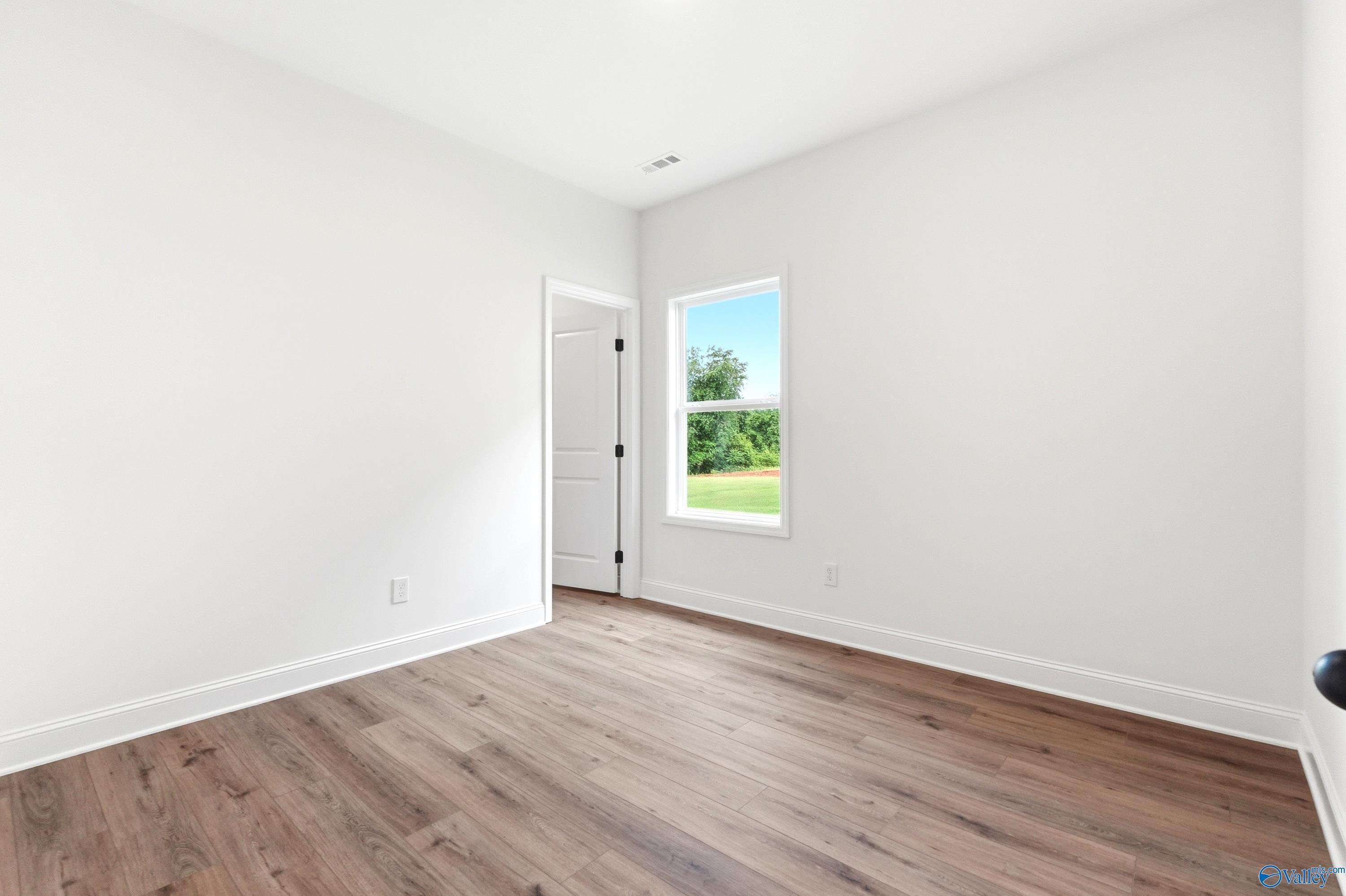 Bright, empty bedroom with wood-look flooring in The Daphne C floor plan at Ivy Hills, Toney, Alabama.