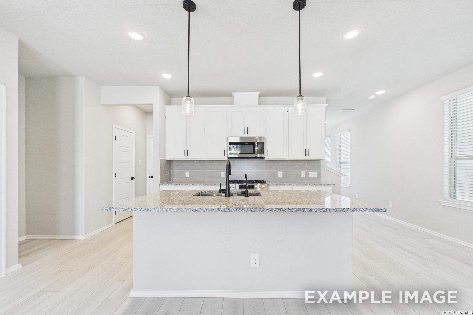 Modern kitchen with white cabinets, granite island, and pendant lighting in Davidson Homes' The Charlotte B in San Antonio.