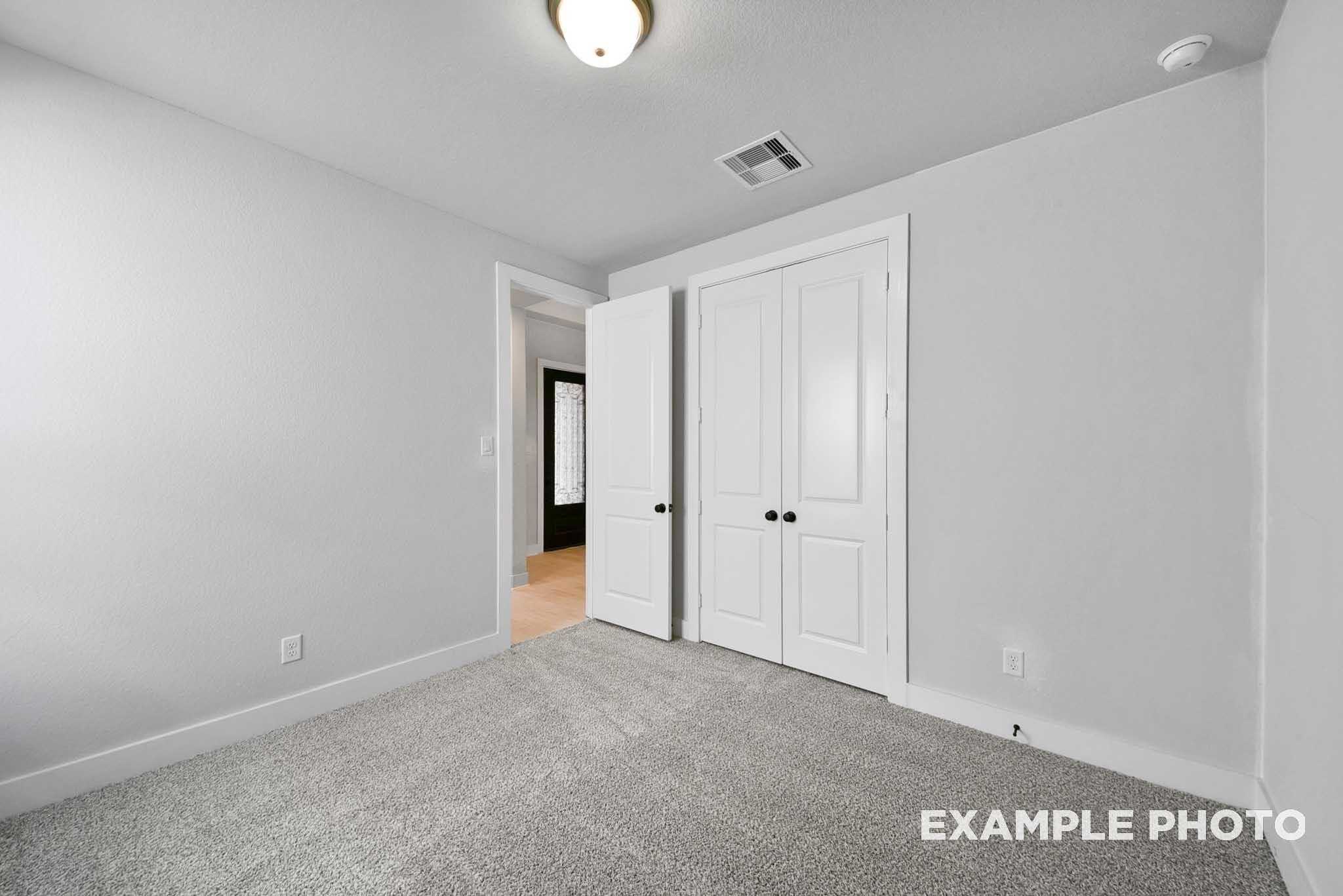 Spacious secondary bedroom with gray walls, plush carpet, double closet doors, and open hallway in Davidson Homes The George A, Lago Mar