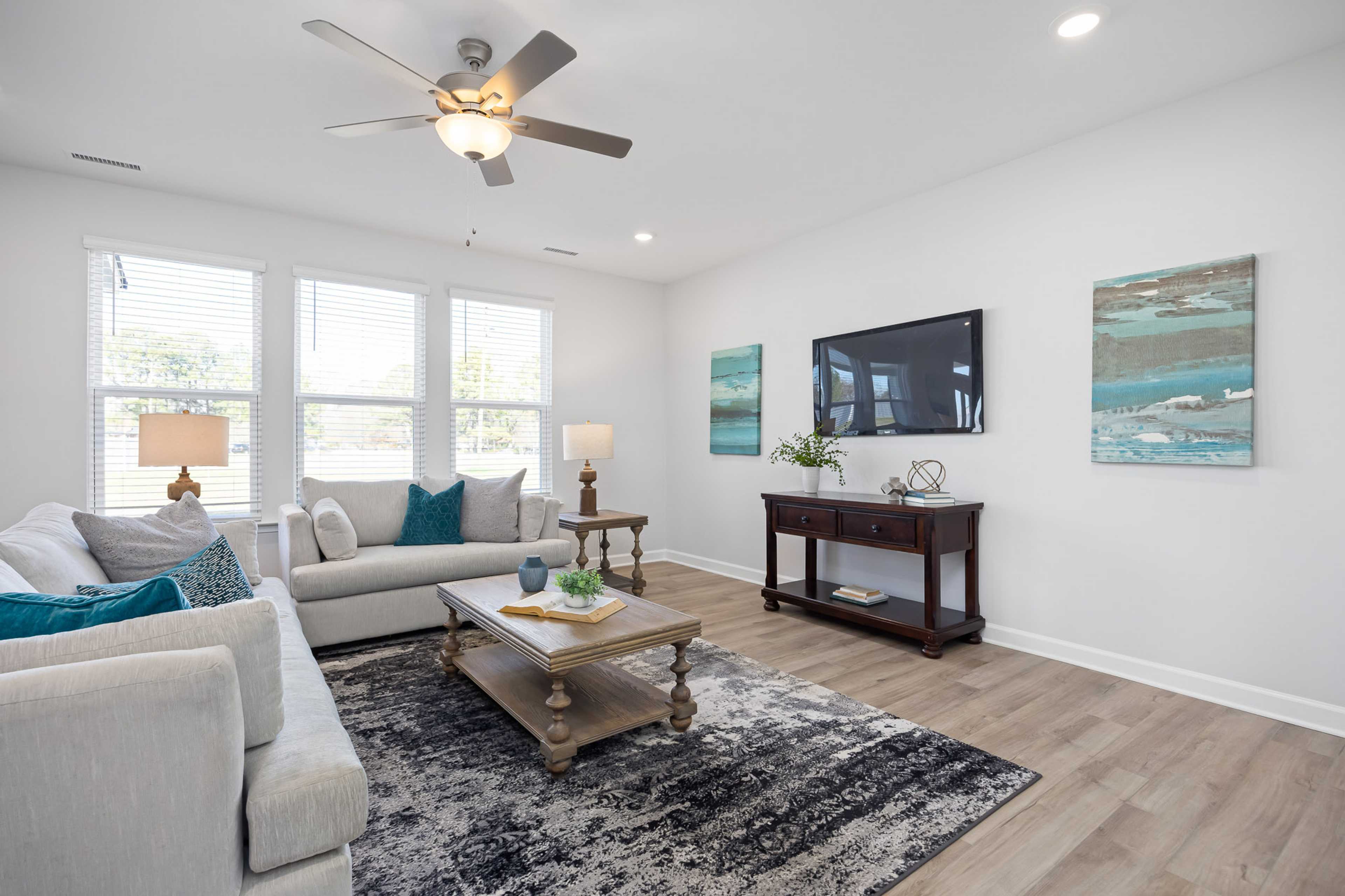 Spacious living room in Stagecoach Corner Mebane NC with gray sectional sofa, teal accents, mounted TV, abstract art, ceiling fan, and hardwood floors
