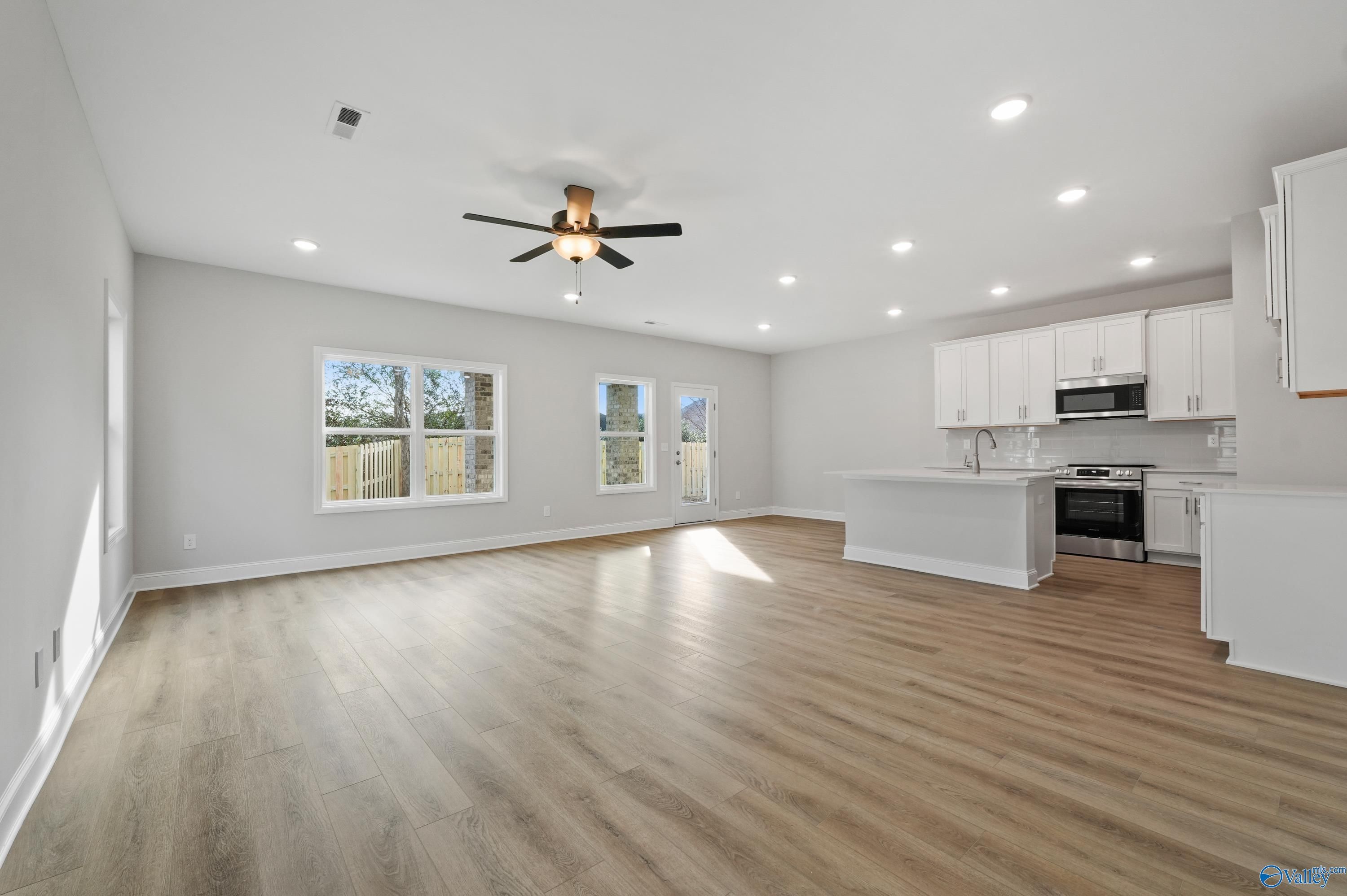 Bright open-concept kitchen with white cabinets, stainless appliances, island, and hardwood floors in The Camden by Davidson Homes, Huntsville