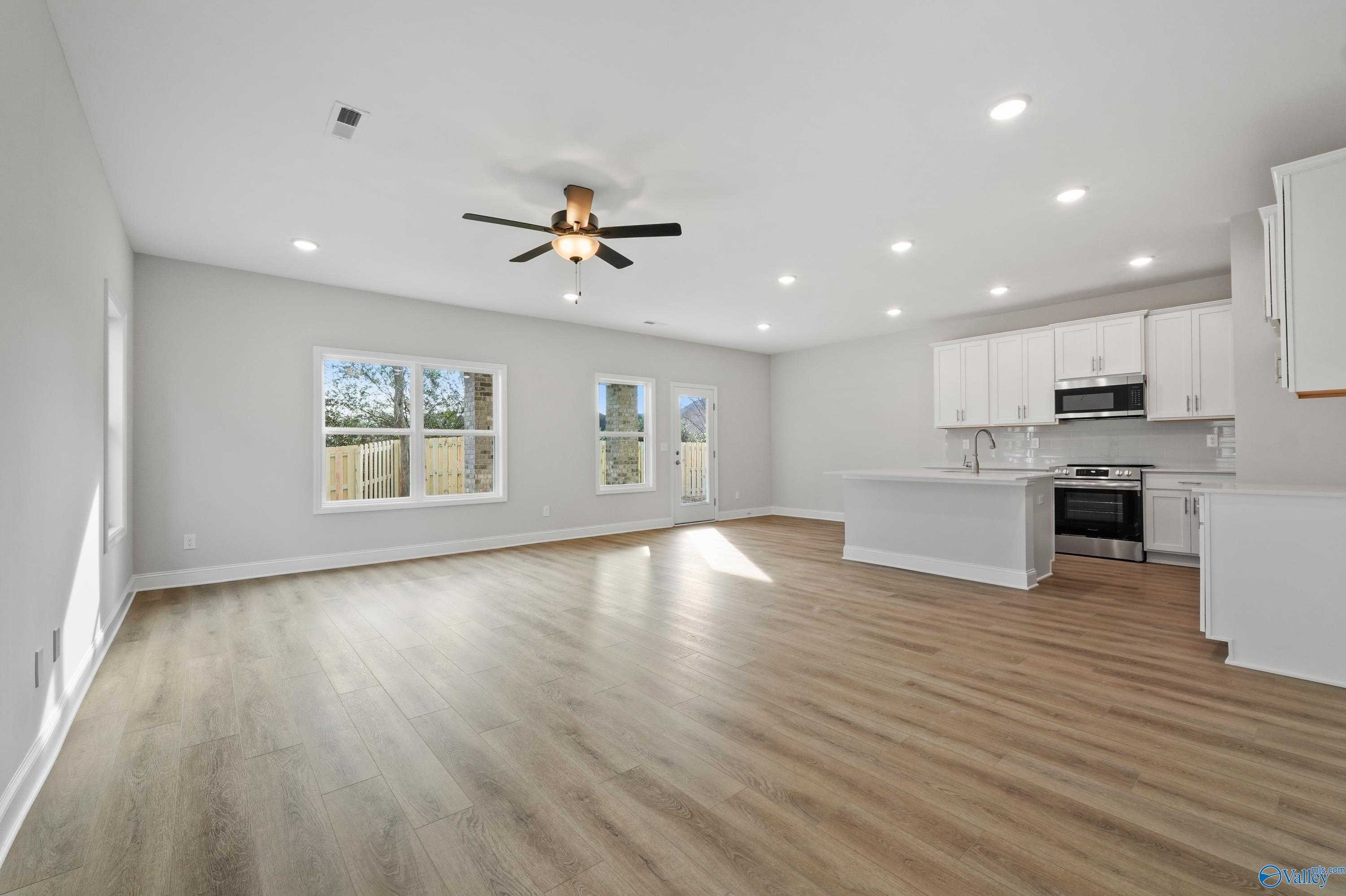 Bright open-concept kitchen with white cabinets, stainless appliances, island, and hardwood floors in The Camden by Davidson Homes, Huntsville