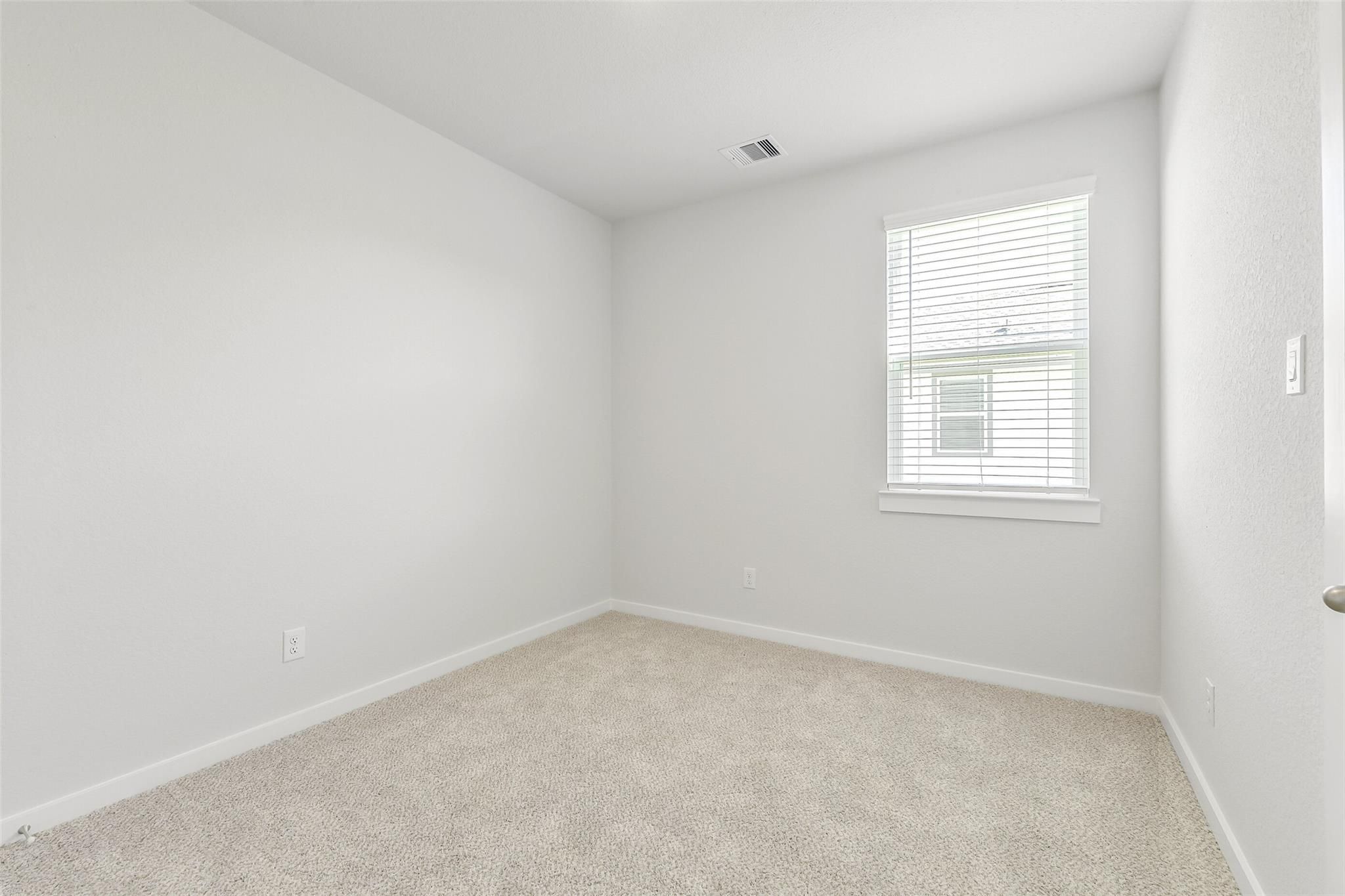 Bright empty bedroom with beige carpet, white walls, and window blinds in 5-bedroom Davidson Homes The San Marcos E, Cleveland, Texas