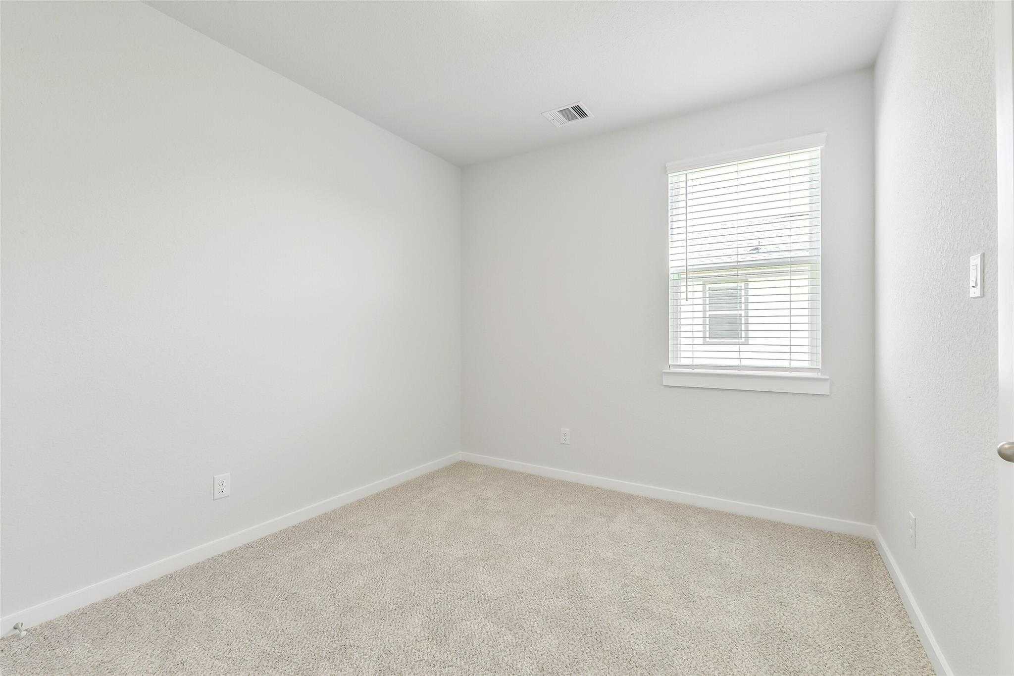 Bright empty bedroom with beige carpet, white walls, and window blinds in 5-bedroom Davidson Homes The San Marcos E, Cleveland, Texas