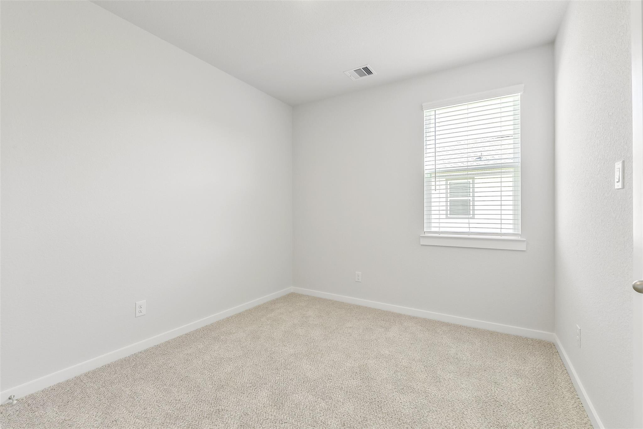 Bright empty bedroom with beige carpet, white walls, and window blinds in 5-bedroom Davidson Homes The San Marcos E, Cleveland, Texas