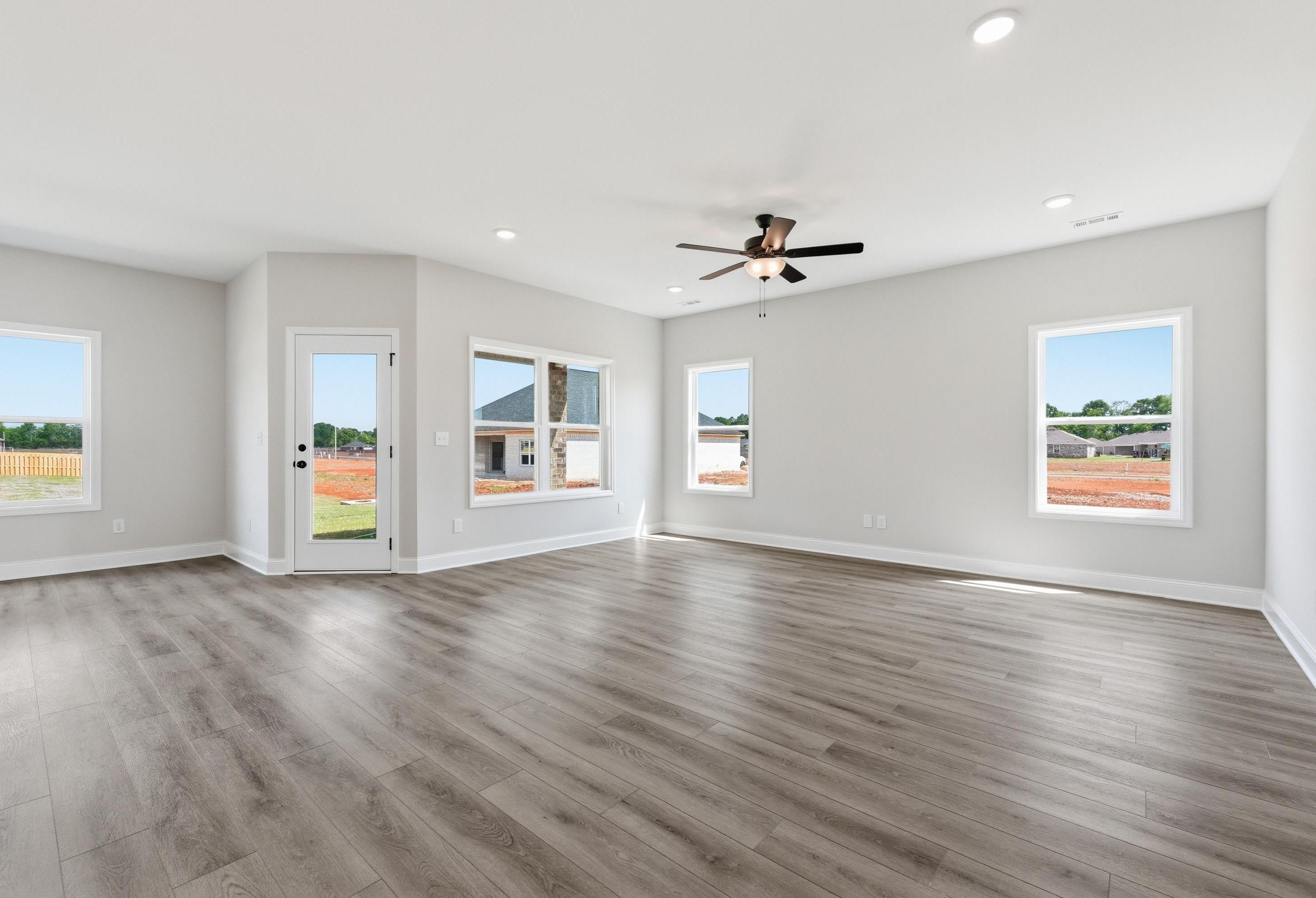 Bright, open-concept living area in The Glen A floor plan featuring wood-style flooring and large windows.