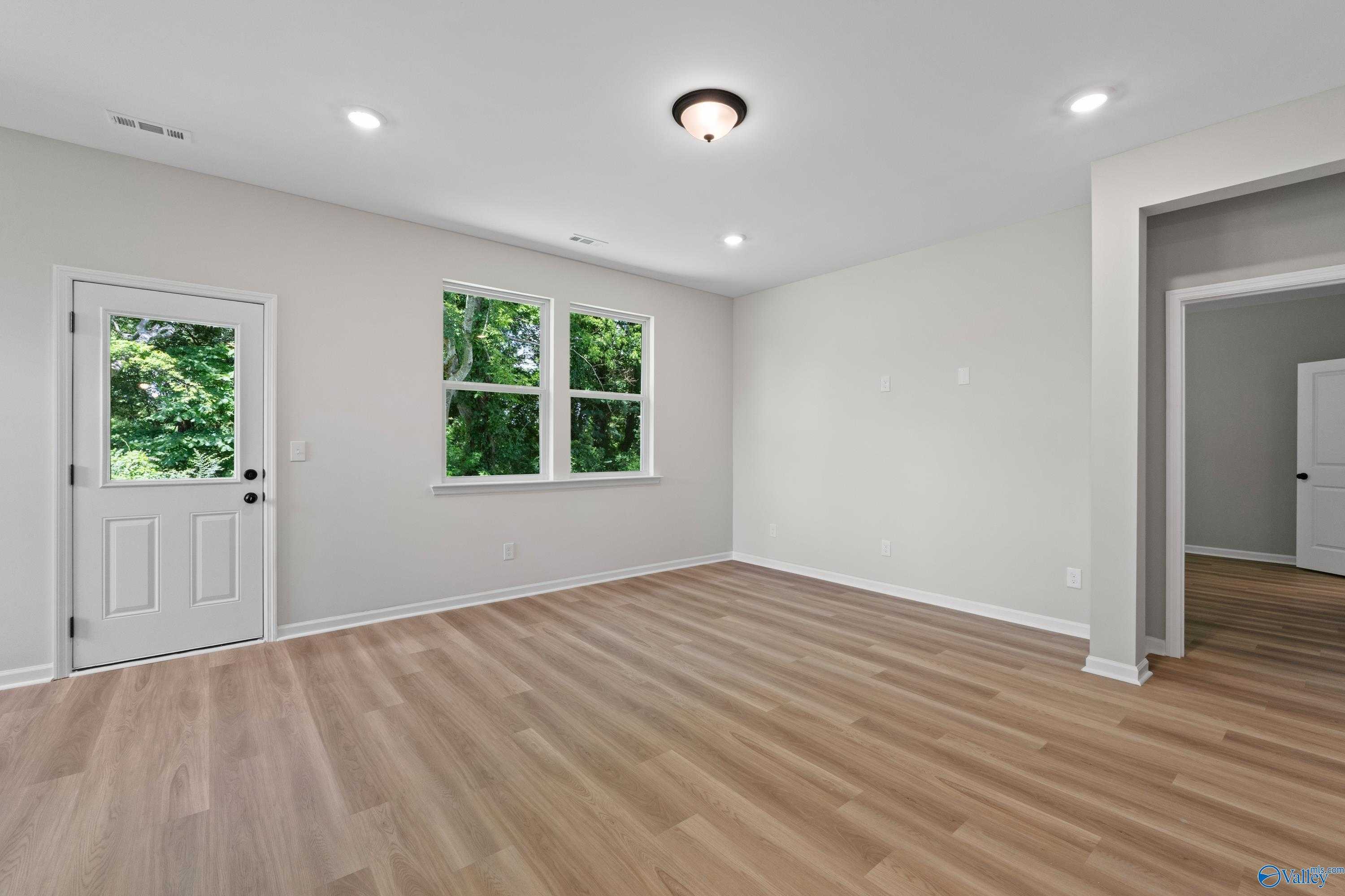 Bright living room with large windows, light hardwood floors, and ceiling fan in Davidson Homes The Phoenix, Hazel Green, Alabama