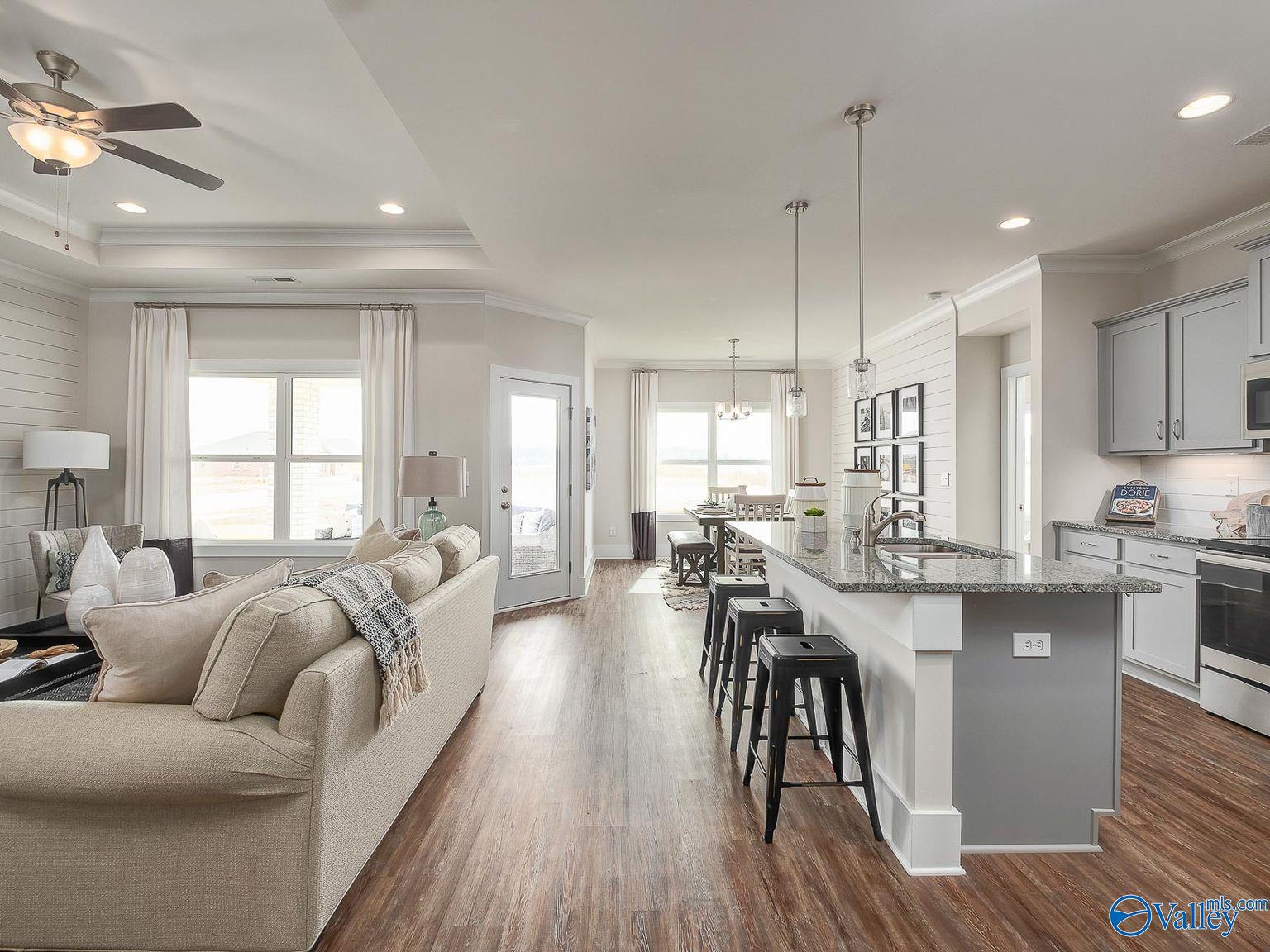 Open-concept living room with beige sofa, dining area, and modern kitchen featuring granite island and bar stools in The Everett home, Toney, Alabama