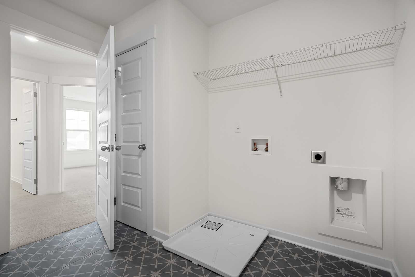 Bright laundry room with wire shelving, washer-dryer hookups, and geometric tiled floor in Davidson Homes The Logan C, Gallatin TN