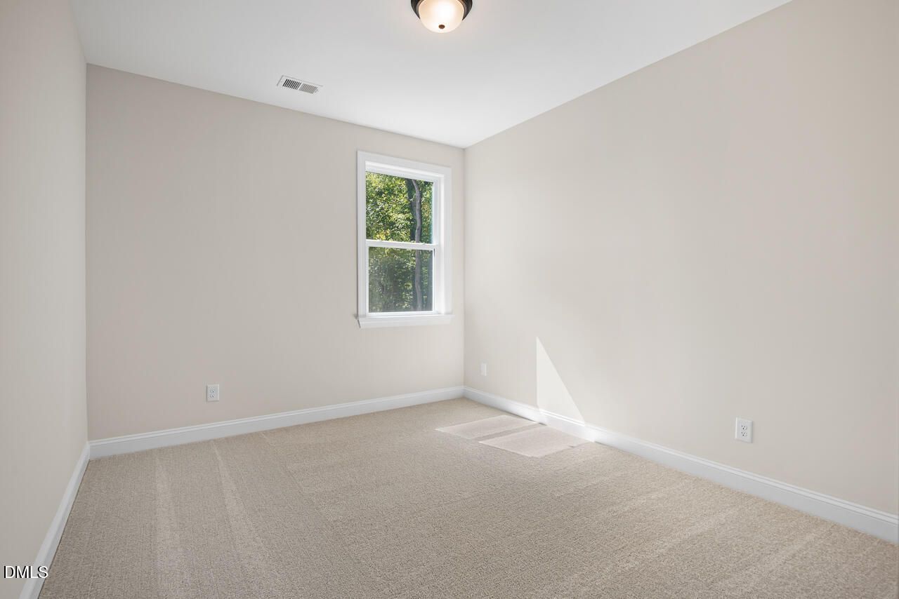 Bright empty bedroom with beige carpet, neutral walls, and window overlooking trees in Davidson Homes Crawford D plan, Wake Forest, NC