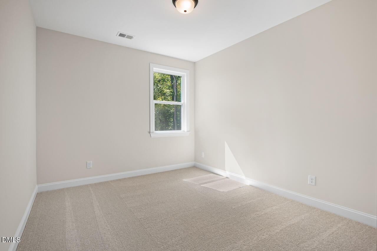 Bright empty bedroom with beige carpet, neutral walls, and window overlooking trees in Davidson Homes Crawford D plan, Wake Forest, NC