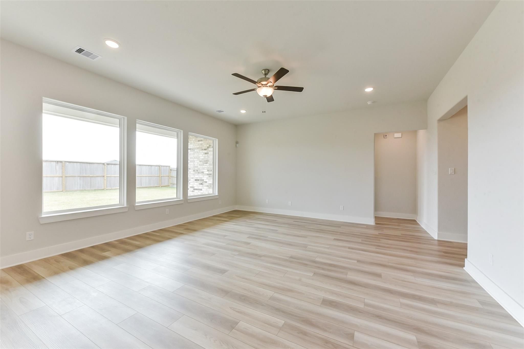 Bright living room with large windows, ceiling fan, and light wood floors in Davidson Homes The Edward A, Lago Mar, Texas City
