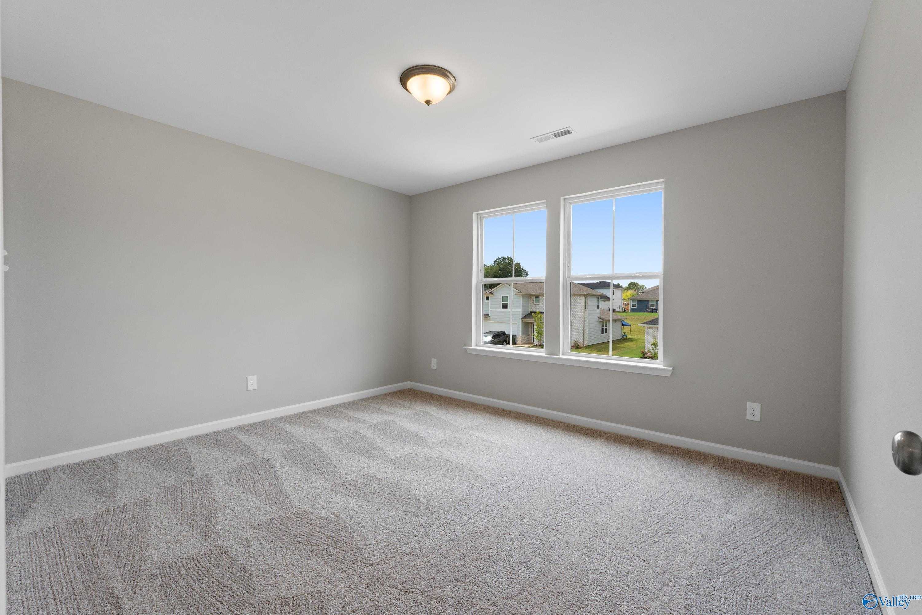 Sunny secondary bedroom with gray walls, plush patterned carpet, and neighborhood views in Evermore Homes The Augusta, Madison, Alabama
