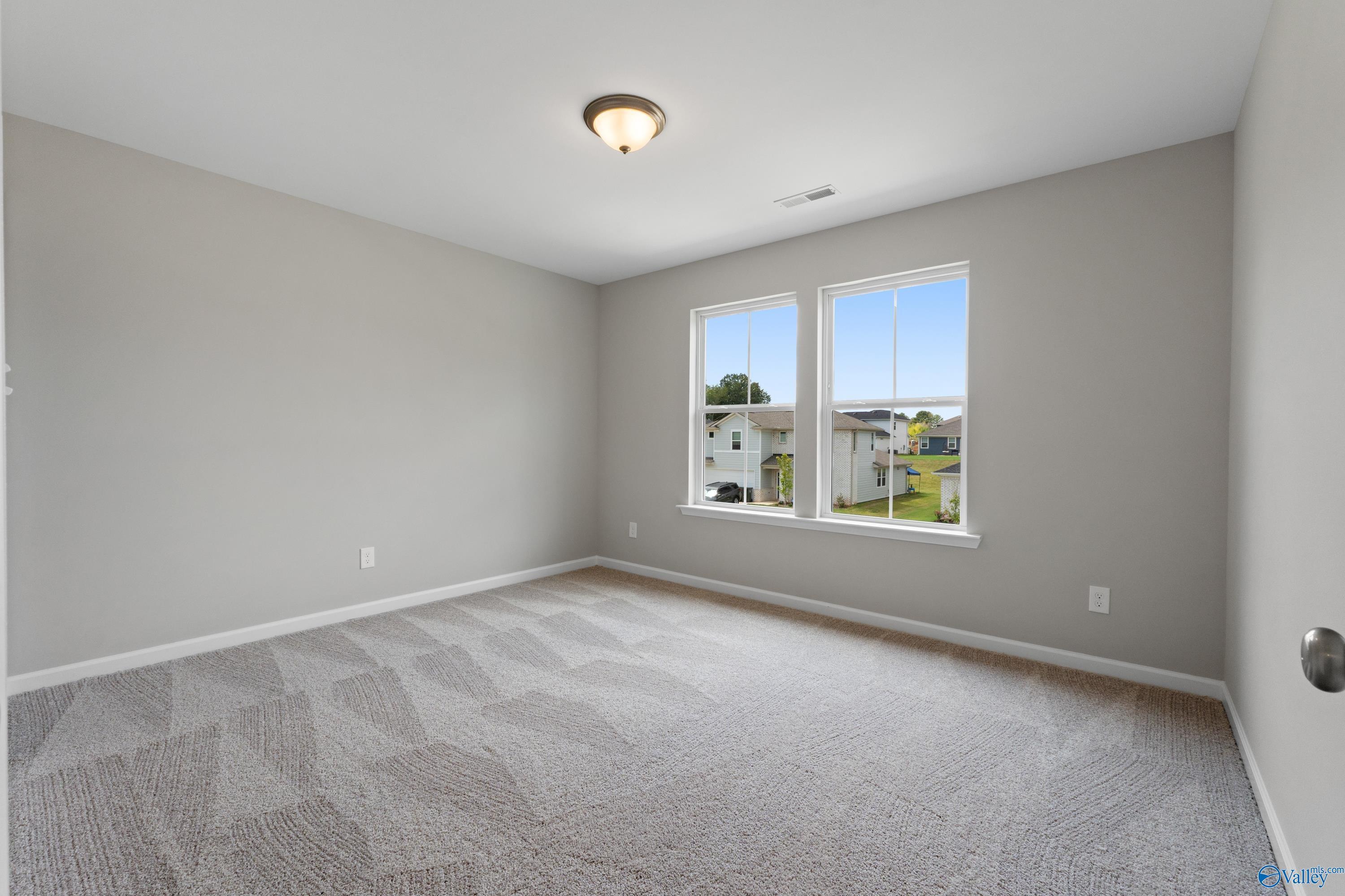 Neutral-toned bedroom with gray walls, patterned carpet, and large windows overlooking neighborhood in Davidson Homes The Augusta, Madison, Alabama