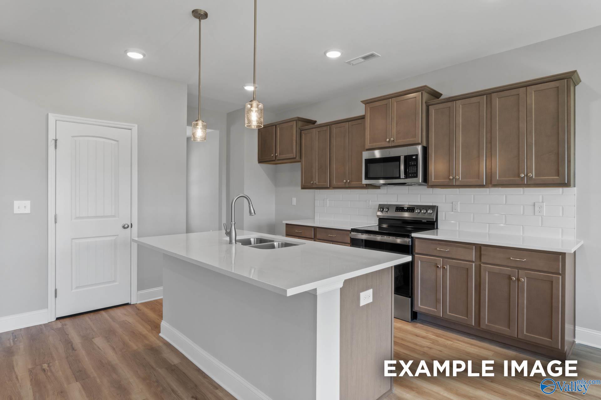 Modern kitchen featuring wood cabinets, white subway tile backsplash, island sink, and stainless appliances in Davidson Homes The Shelby B, New Market, Alabama