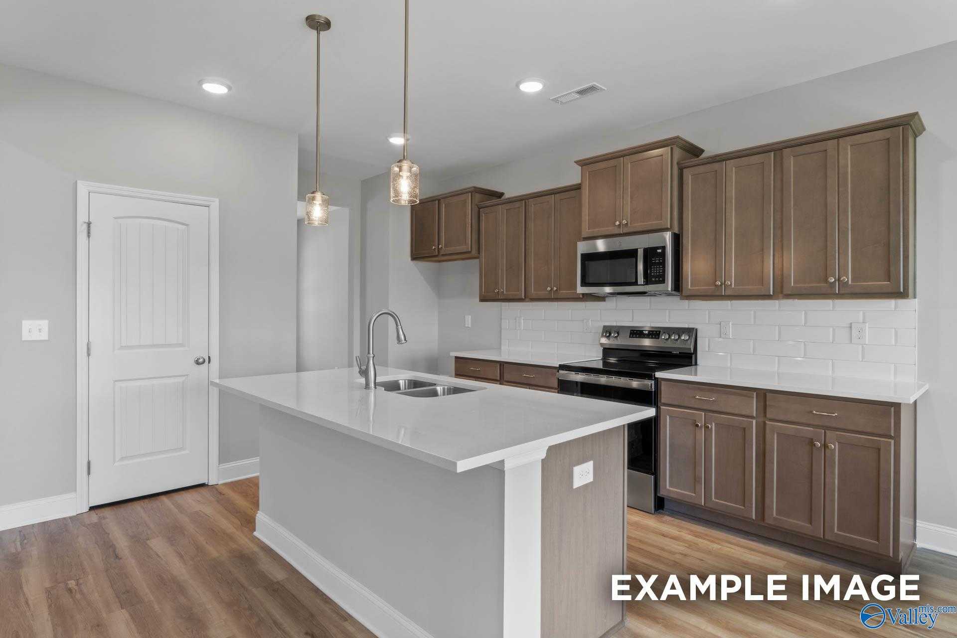 Modern kitchen featuring wood cabinets, white subway tile backsplash, island sink, and stainless appliances in Davidson Homes The Shelby B, New Market, Alabama