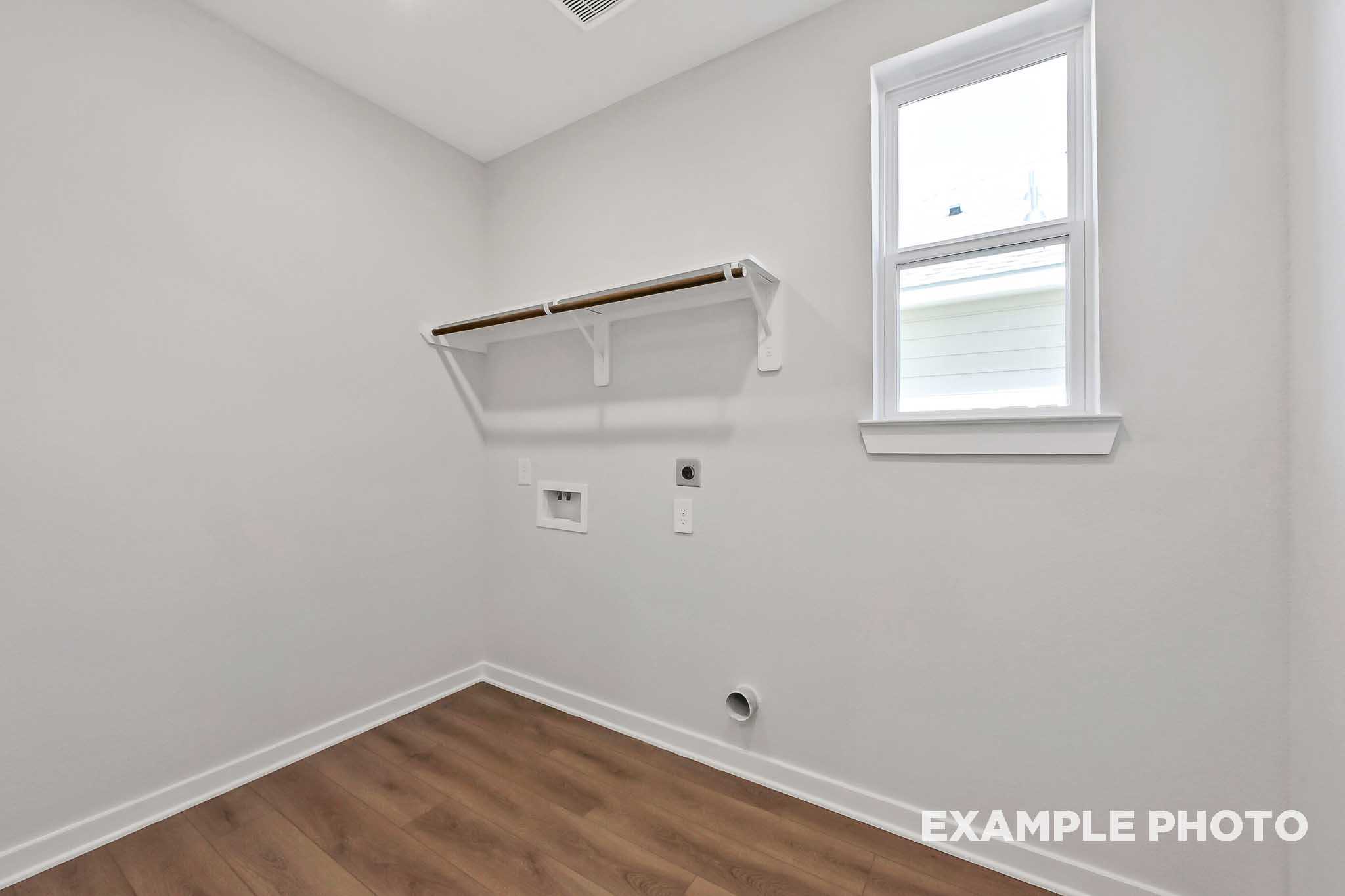 Spacious laundry room in The Sequoia home plan featuring white walls, wooden shelves, washer dryer hookups, and hardwood flooring