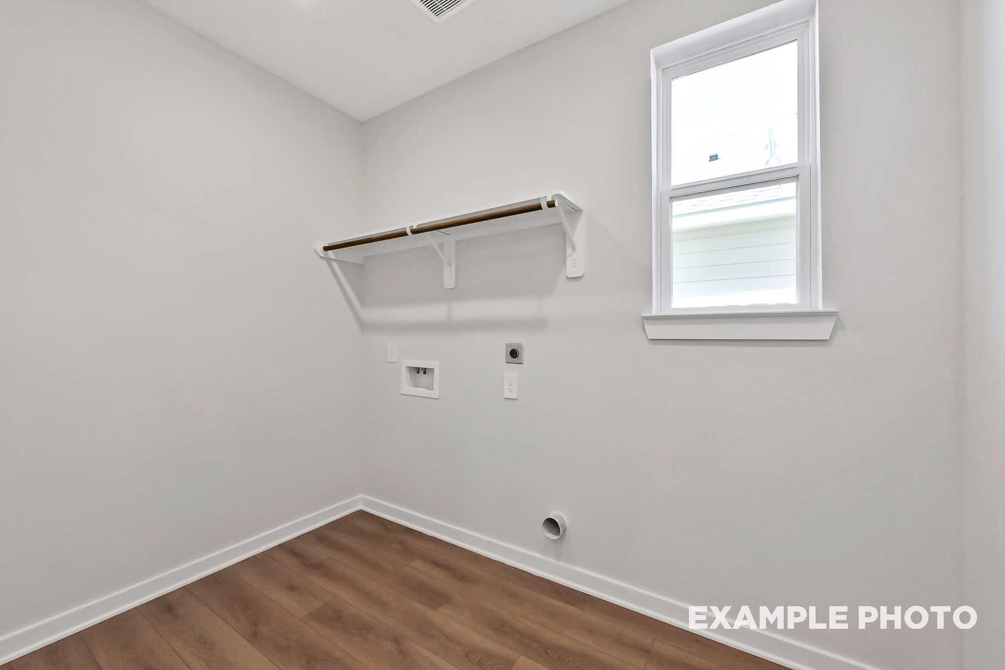 Spacious laundry room in The Sequoia home plan featuring white walls, wooden shelves, washer dryer hookups, and hardwood flooring