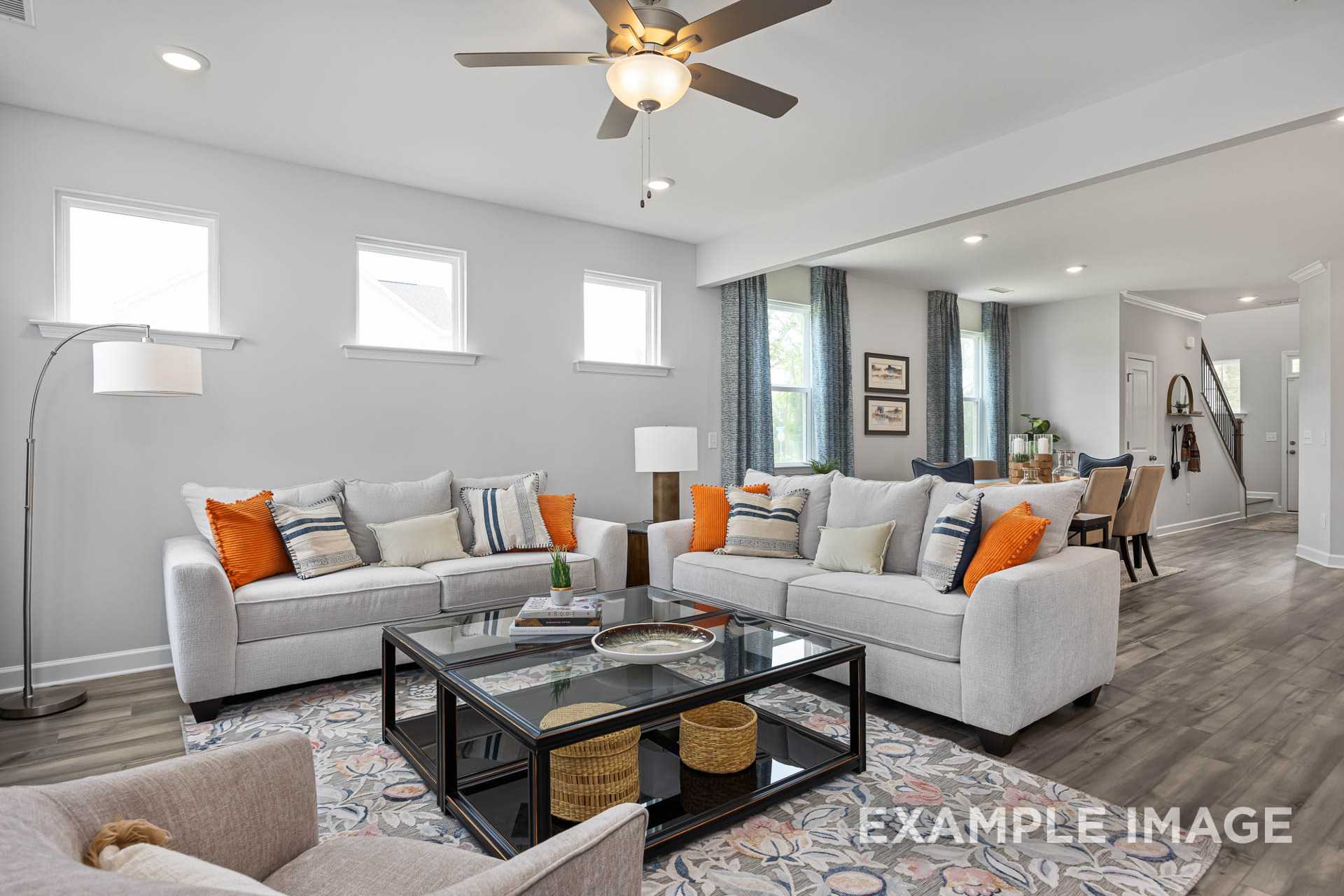 Spacious living room in The Adalynn A by Davidson Homes featuring neutral sofas, glass coffee table, ceiling fan, and open dining in Lillington NC