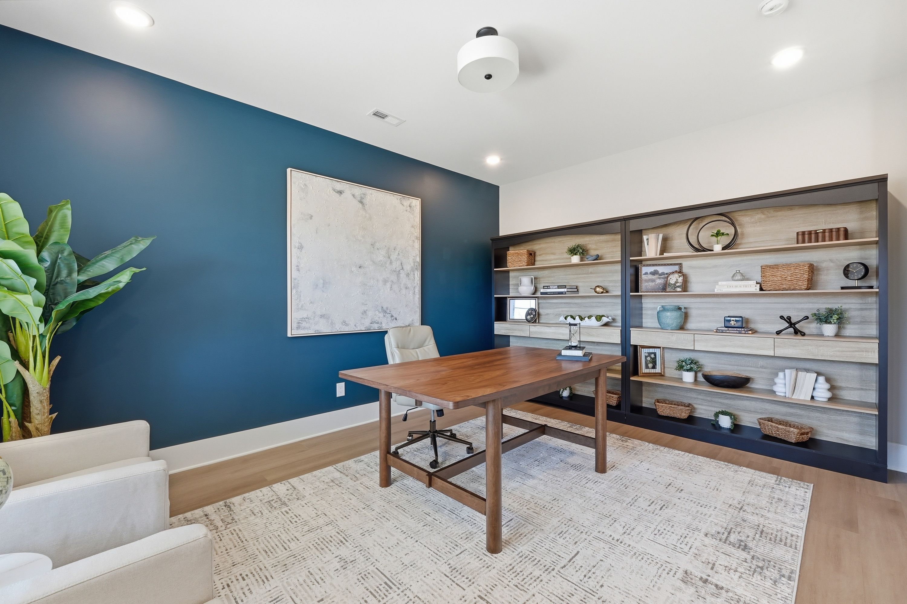 Cozy home office in Berry Cove, New Market AL by Davidson Homes featuring wooden desk, built-in bookshelves, navy wall, and potted plant