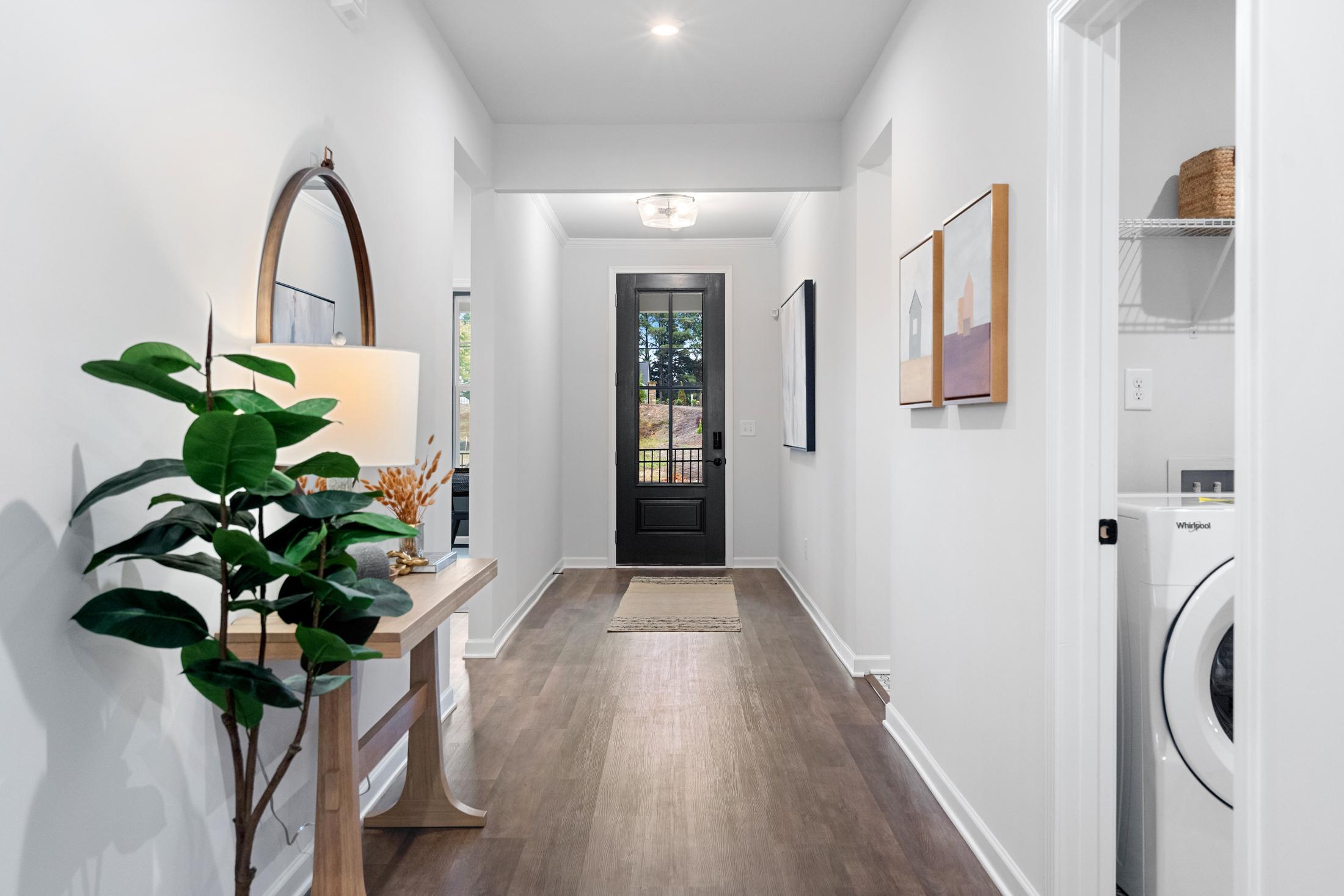 Spacious hallway in The Edison A home with wood floors, entry console table, potted plant, artwork, and adjacent laundry room